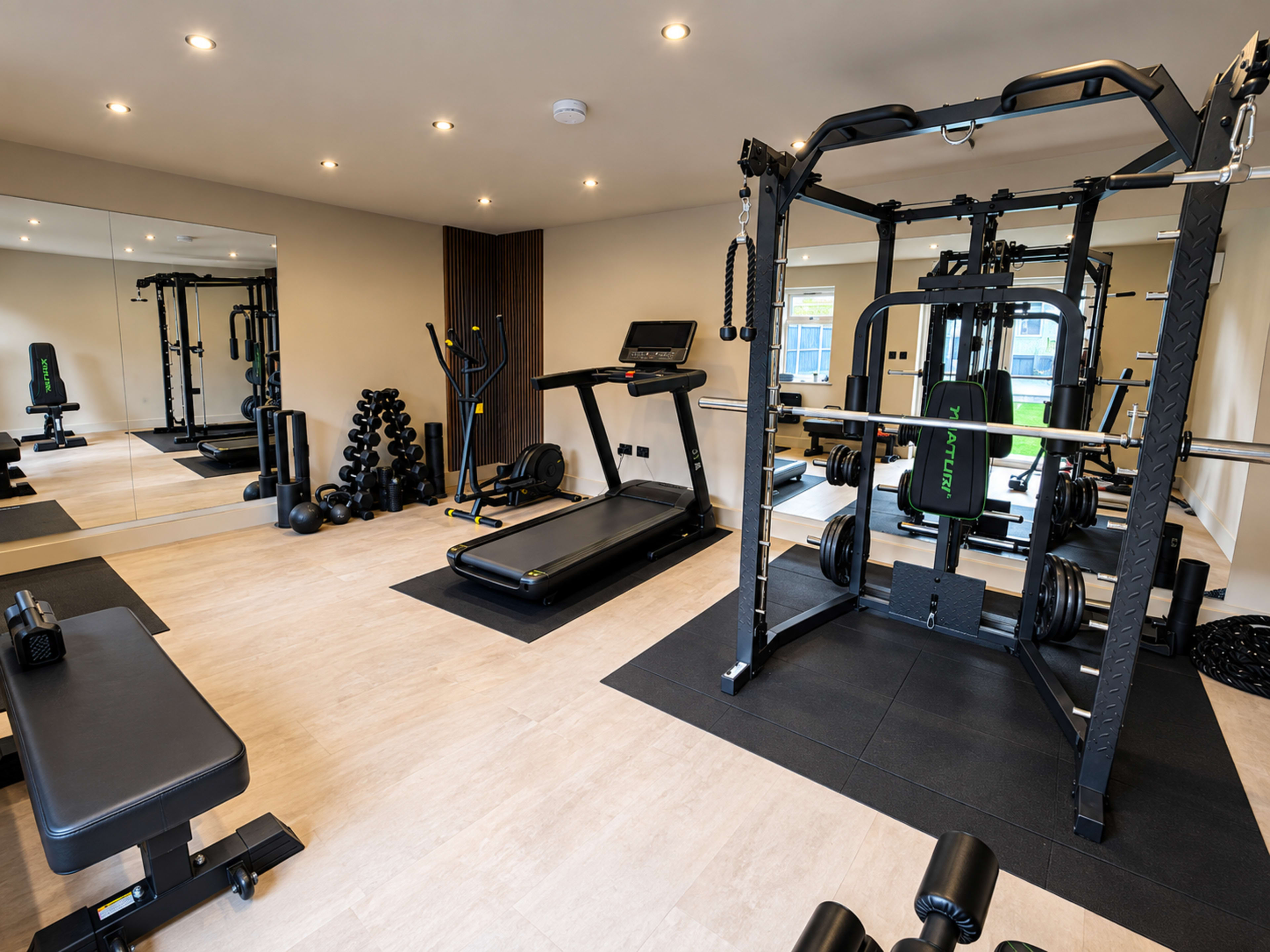 The image shows a spacious home gym equipped with a treadmill, weight bench, multi-station weight machine, and free weights.