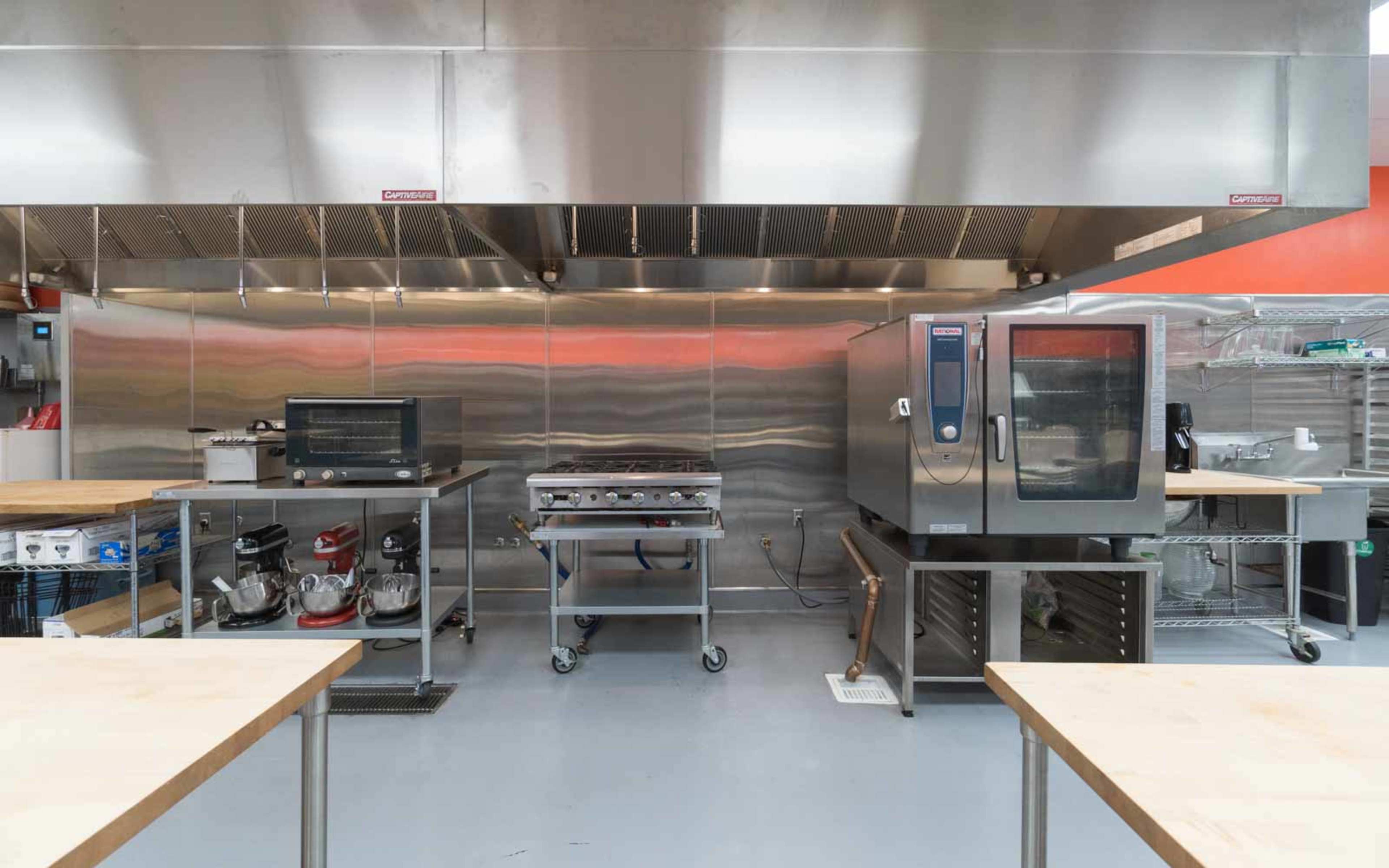 A modern kitchen equipped with various appliances, including a microwave, a griddle, and a convection oven, set against a sleek stainless steel backdrop.
