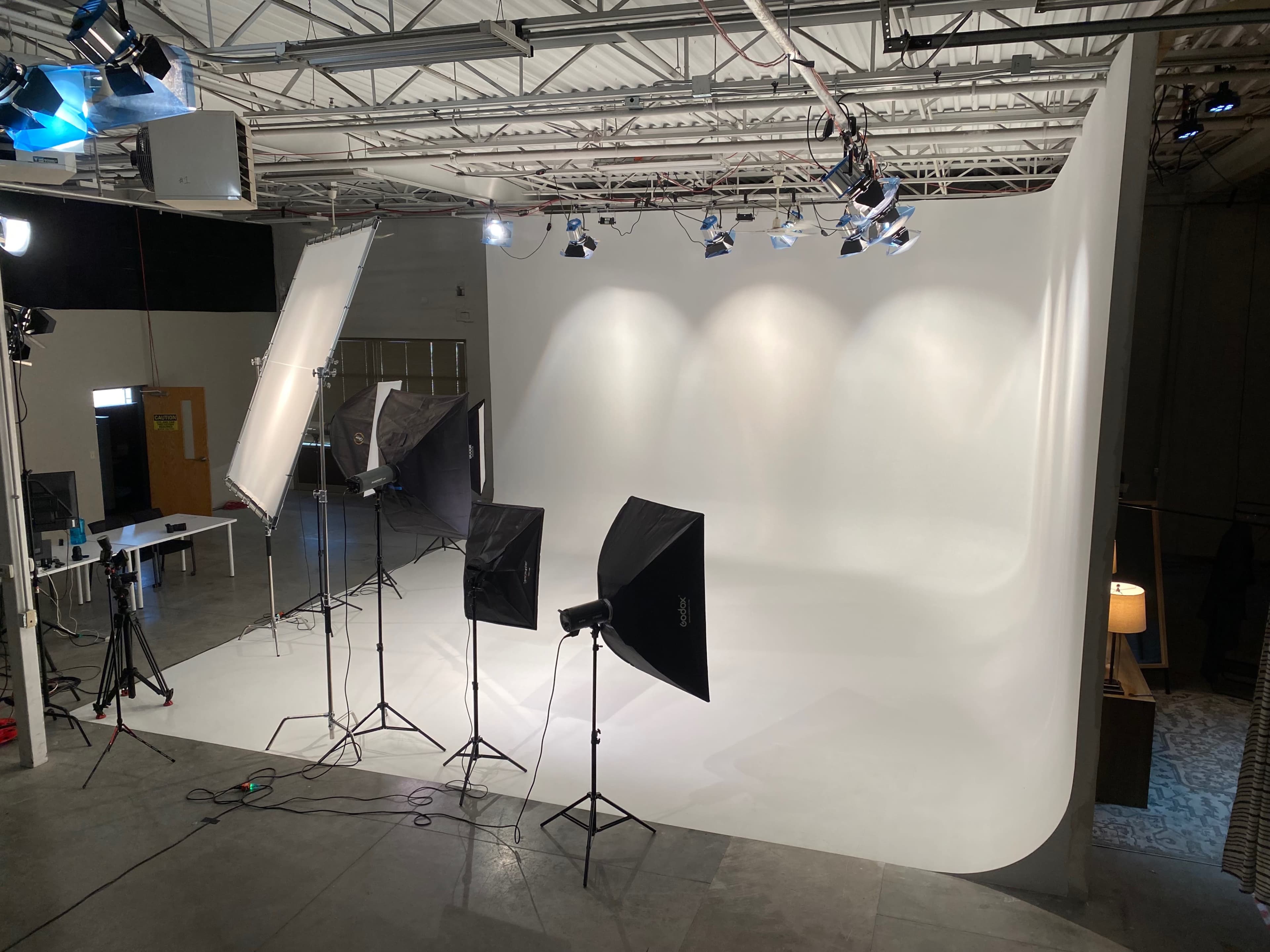 A photography studio features a seamless white backdrop, several light sources, and equipment set up for a photoshoot.