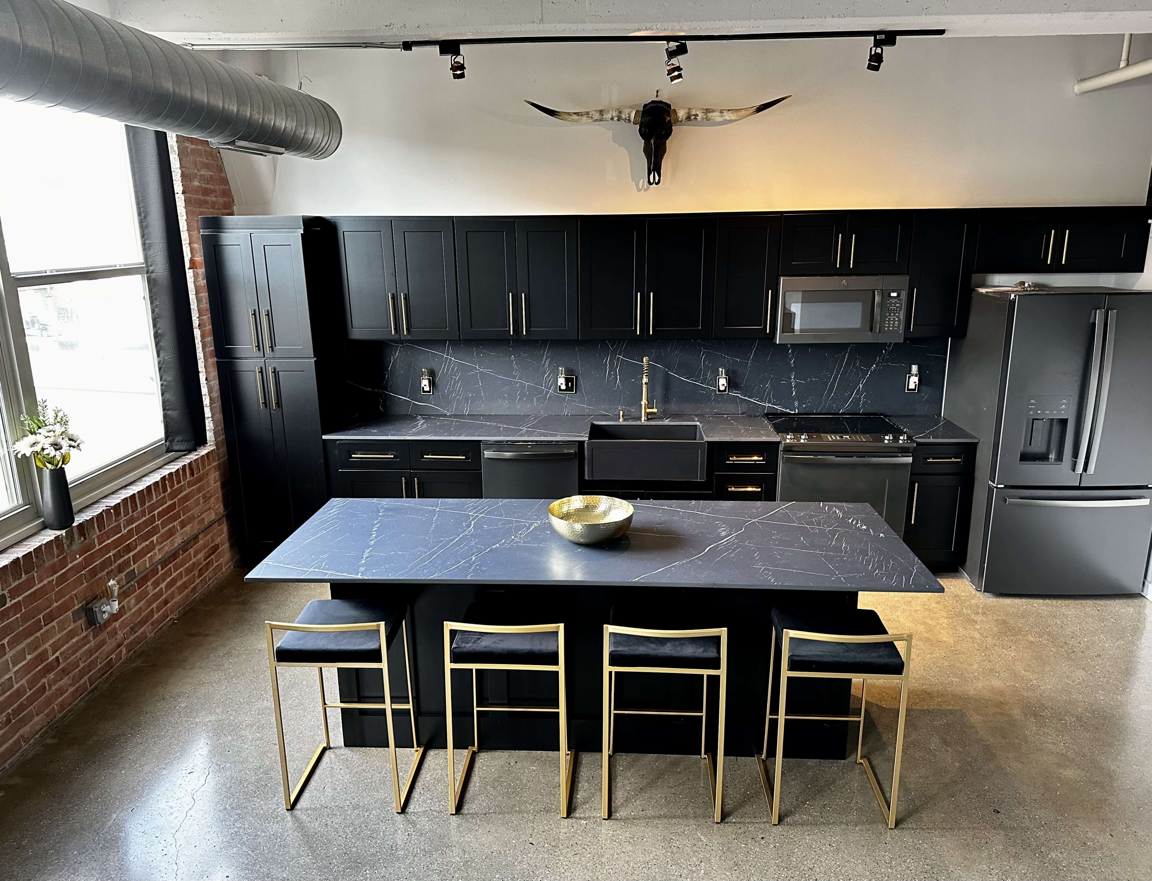 A modern kitchen with black cabinetry, a marble countertop, and gold-accented bar stools arranged around a large island.