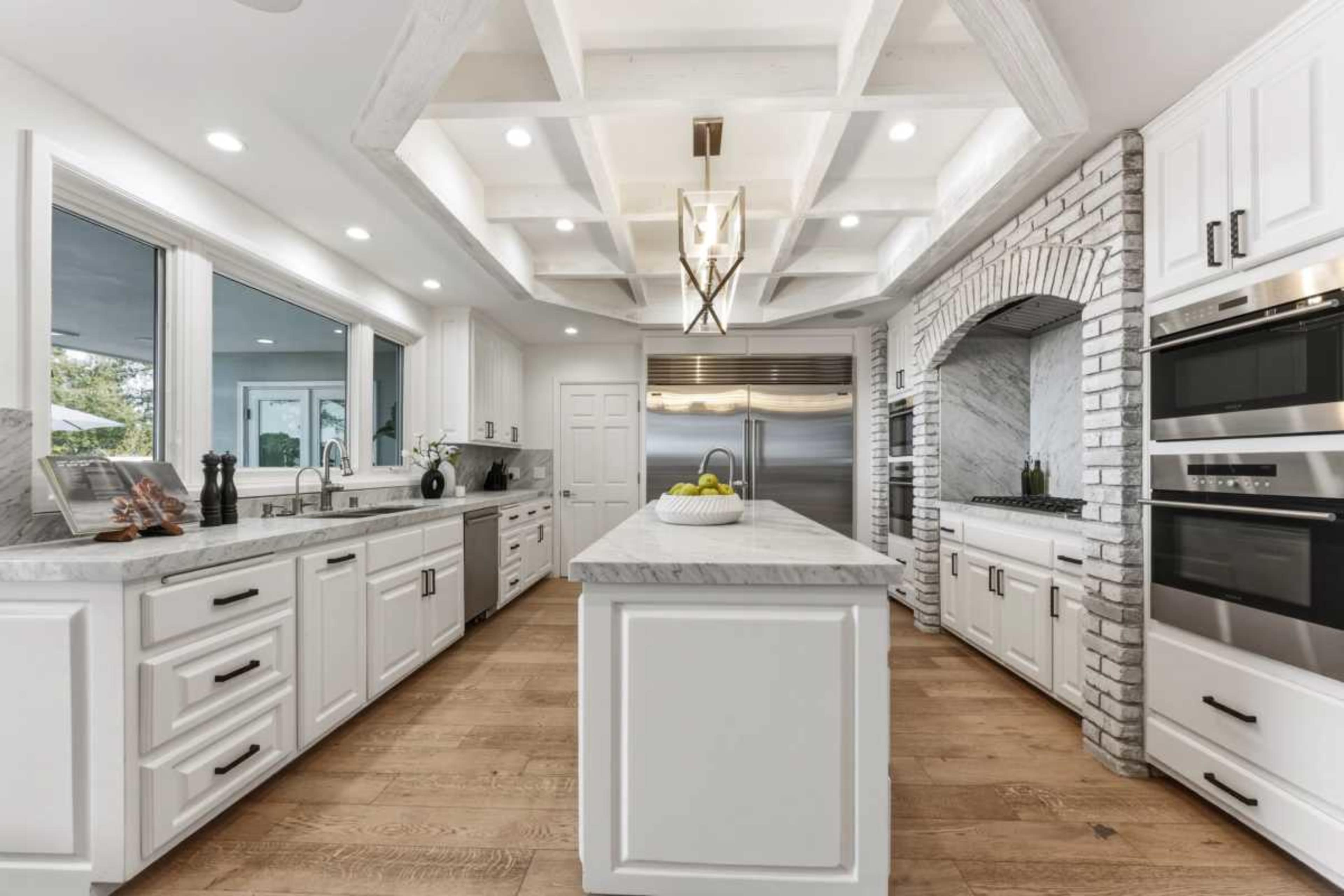 A modern kitchen features white cabinetry, stainless steel appliances, and a large central island with marble countertop.