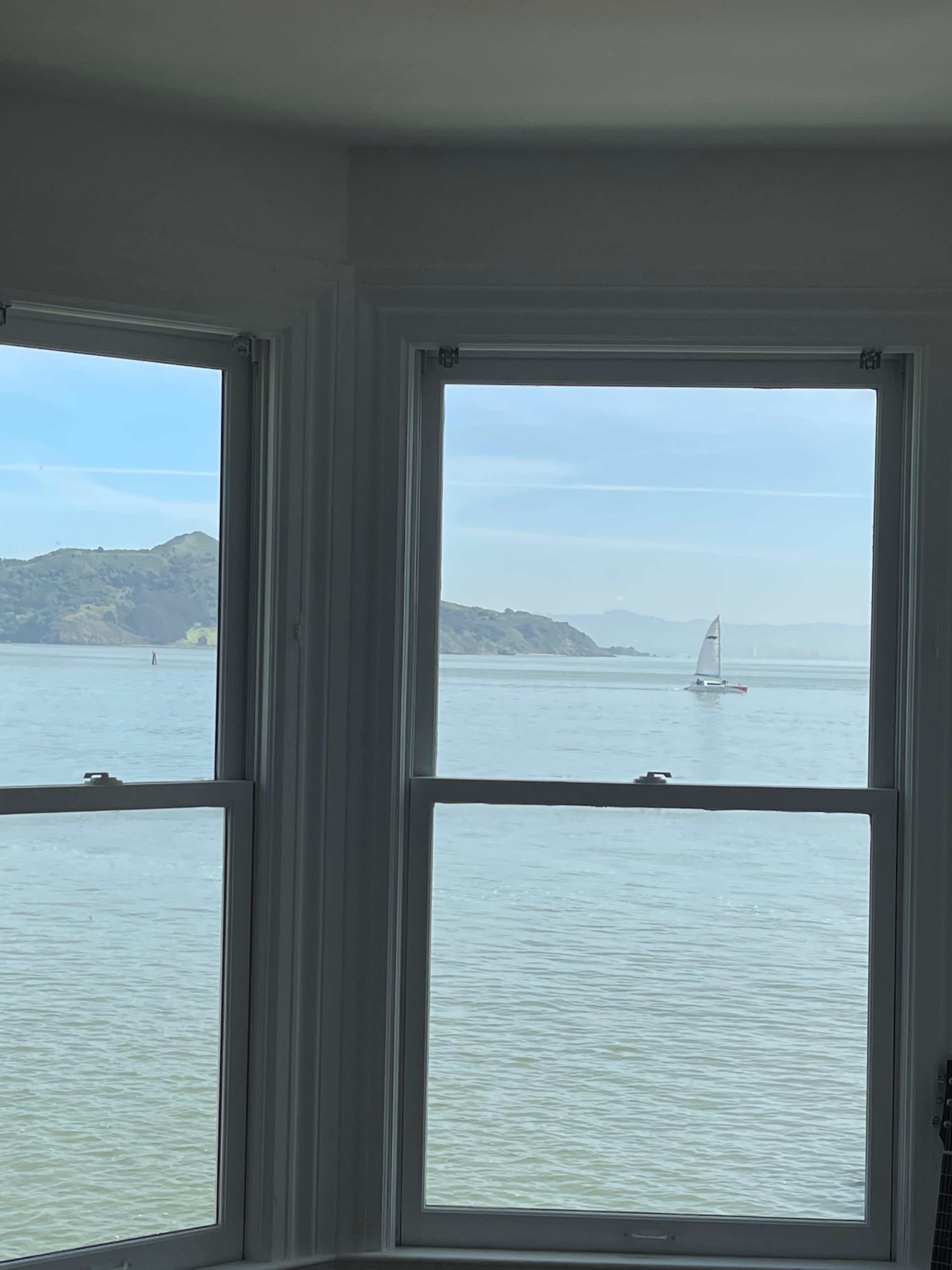 A sailboat is visible on the water, framed by two large windows with a view of hills in the background.