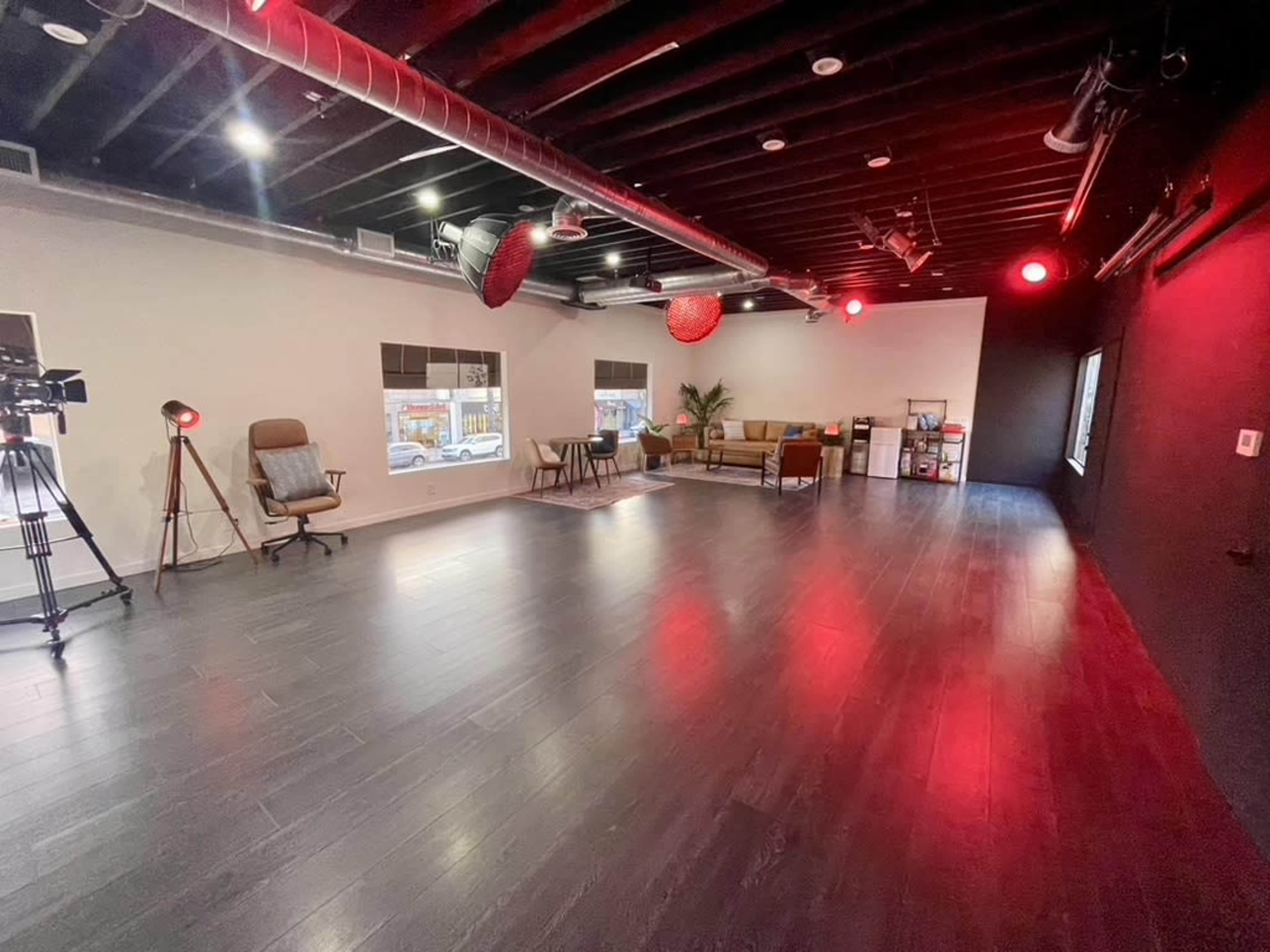 A spacious, well-lit studio with dark wooden flooring, modern furniture, and cameras set up for a production.