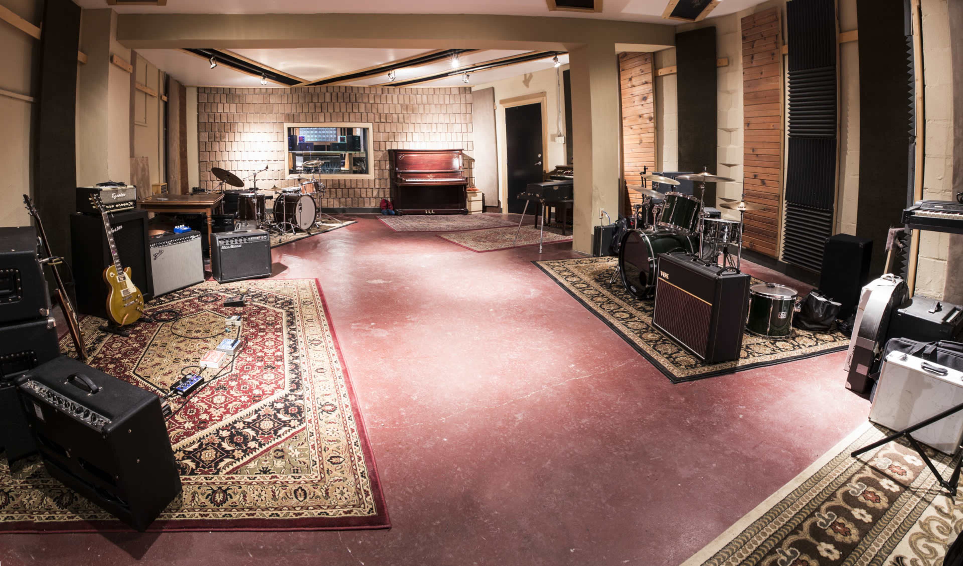 A well-equipped music studio features various instruments, amplifiers, and sound equipment arranged on patterned rugs.