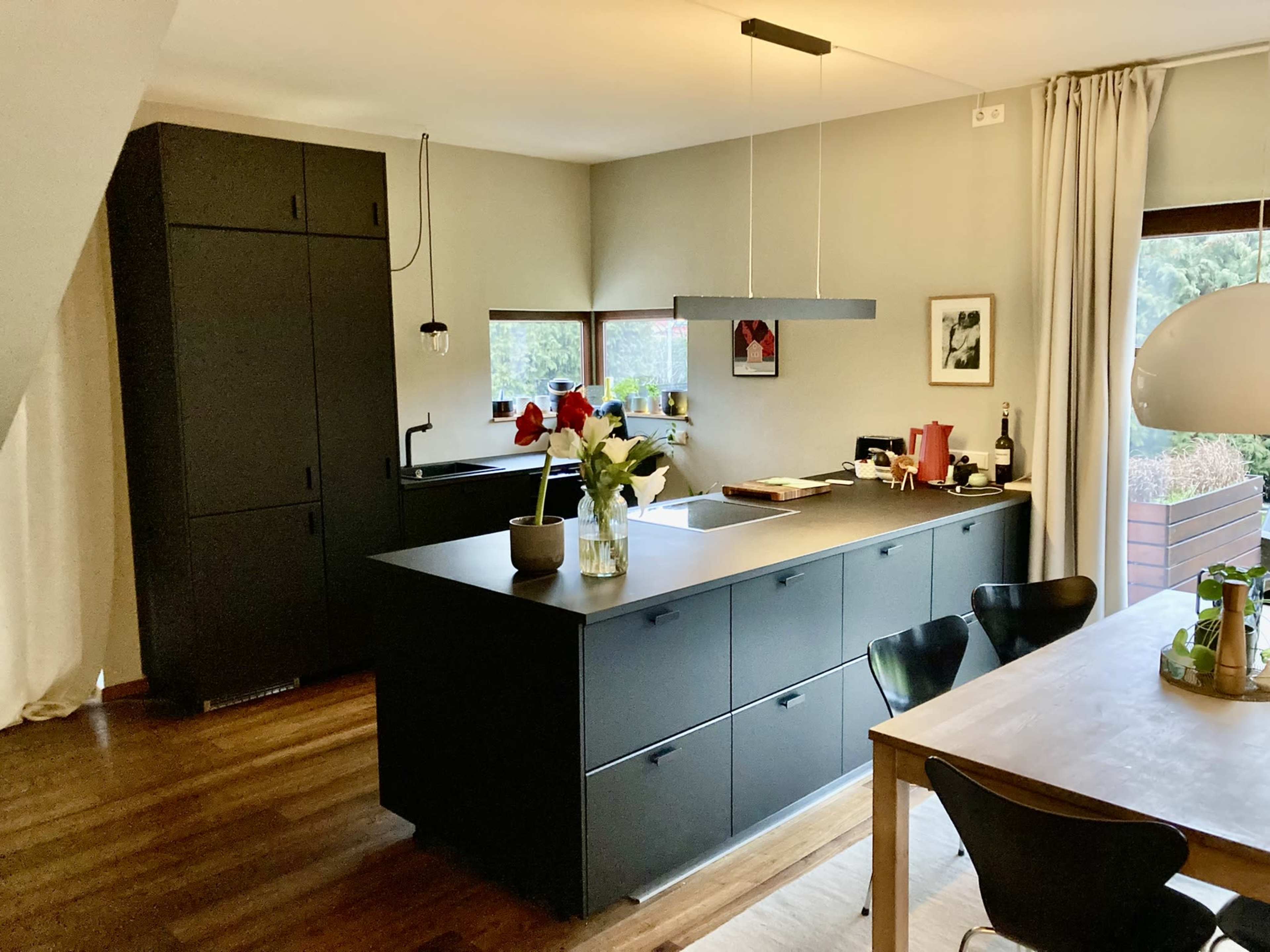 A modern kitchen with black cabinetry, a central island, and a wooden dining table.