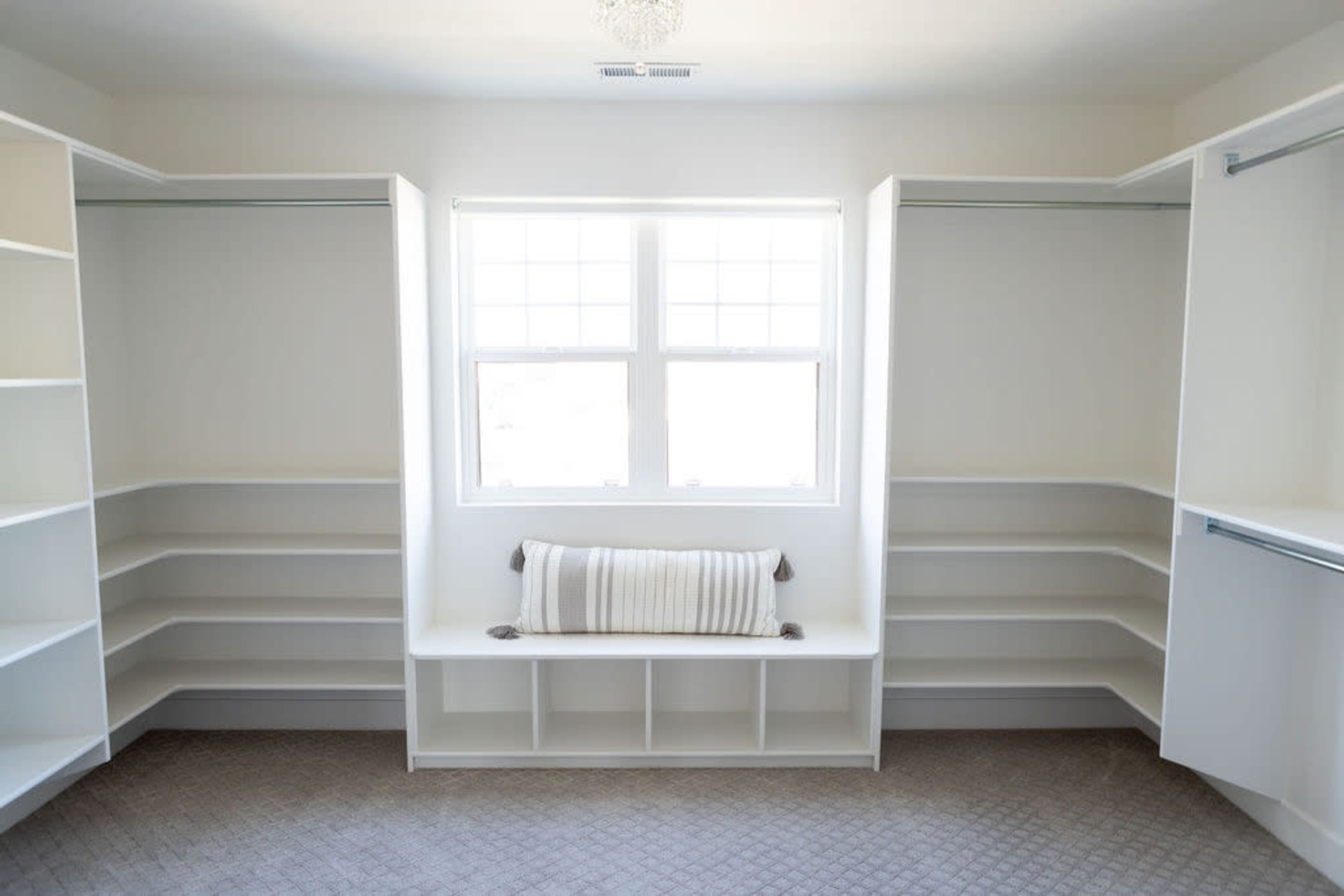 A spacious, empty walk-in closet with built-in white shelving and a window letting in natural light.