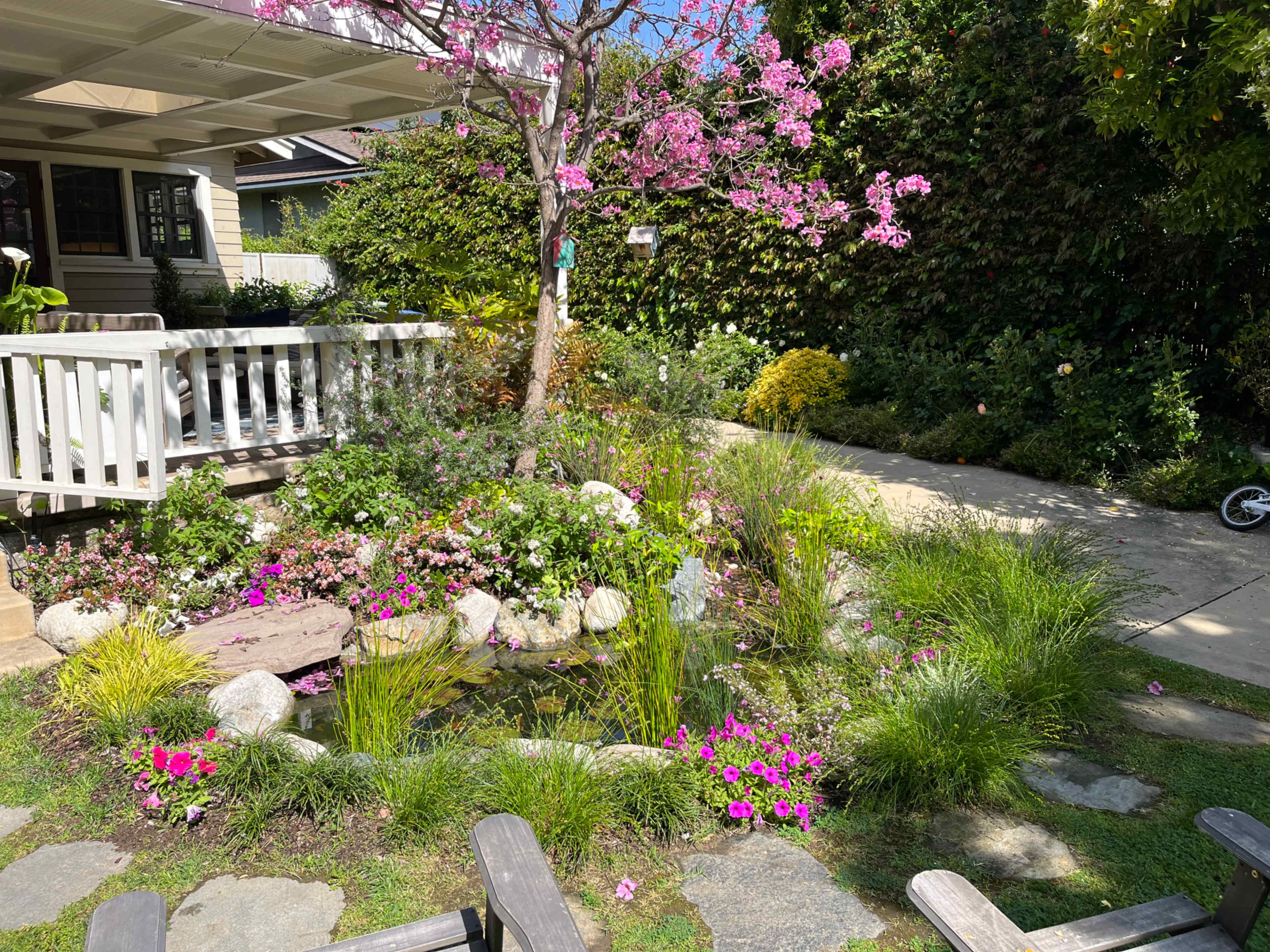 A garden area filled with various colorful flowers, a small pond surrounded by rocks, and a path leading to a house.