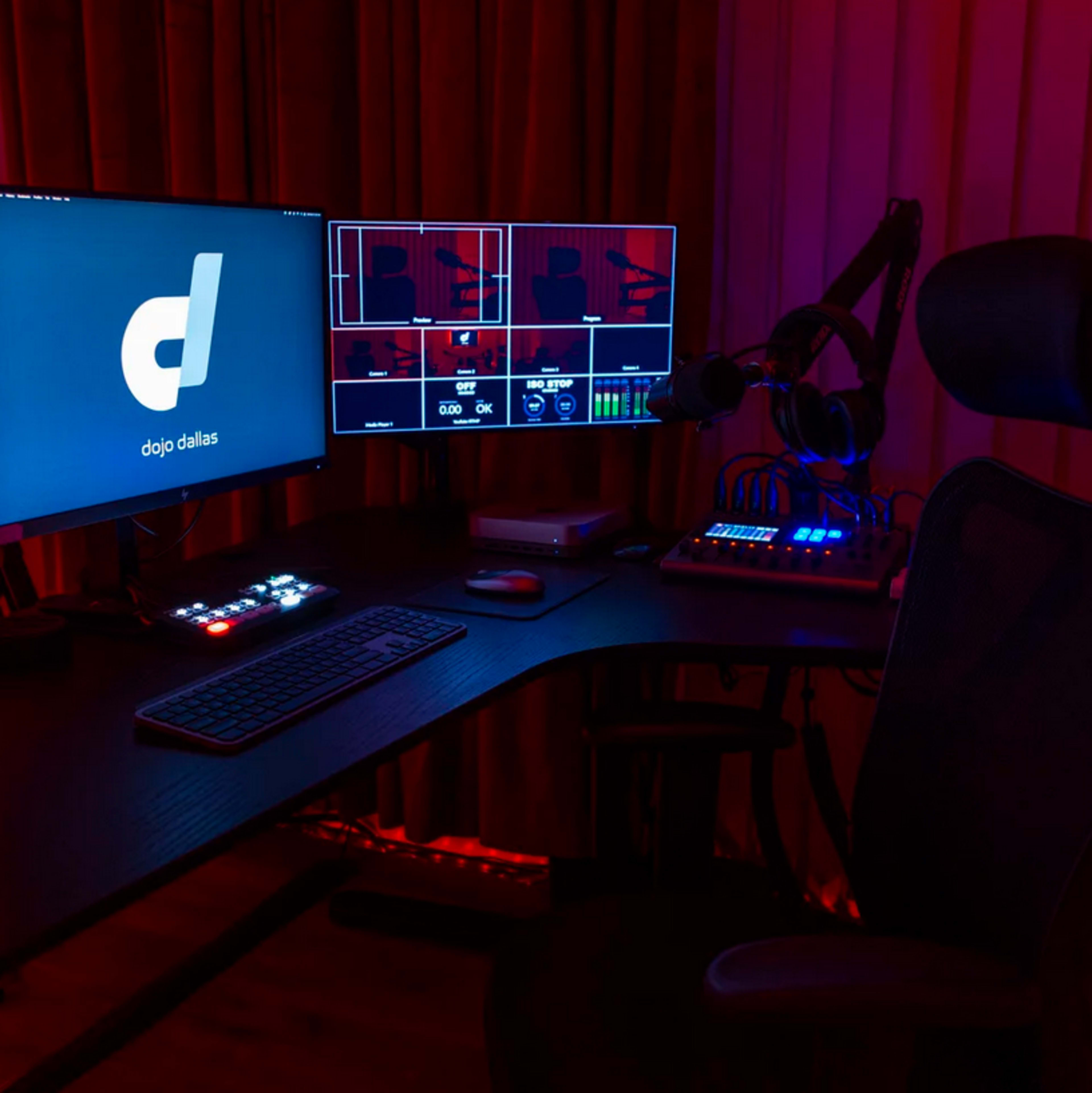 A modern workspace is set up with two monitors displaying a software interface and a logo, surrounded by colorful lighting and audio equipment.