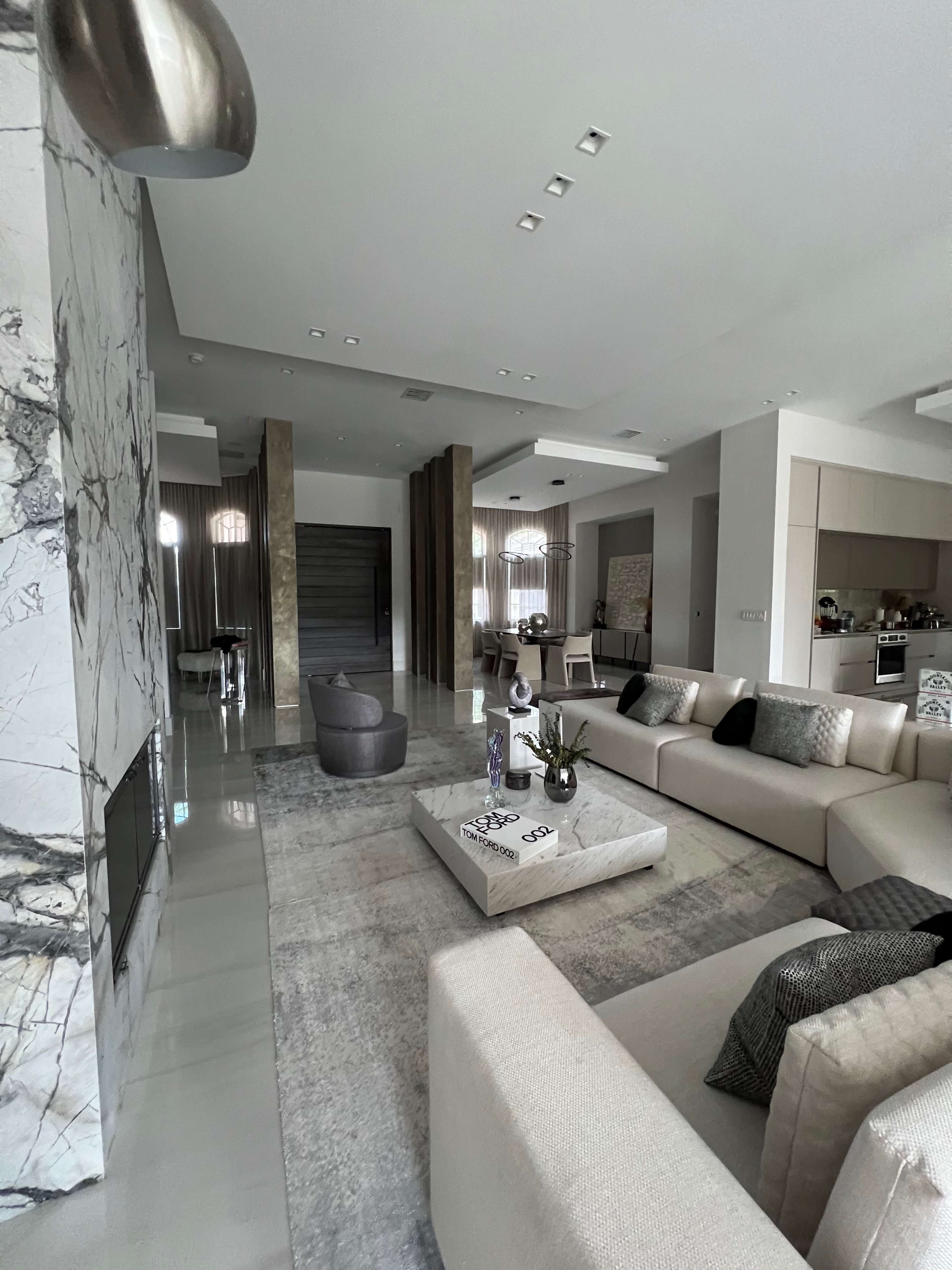 A modern living room with a large sectional sofa, a coffee table, and a sleek fireplace, accented by marble and neutral color tones.
