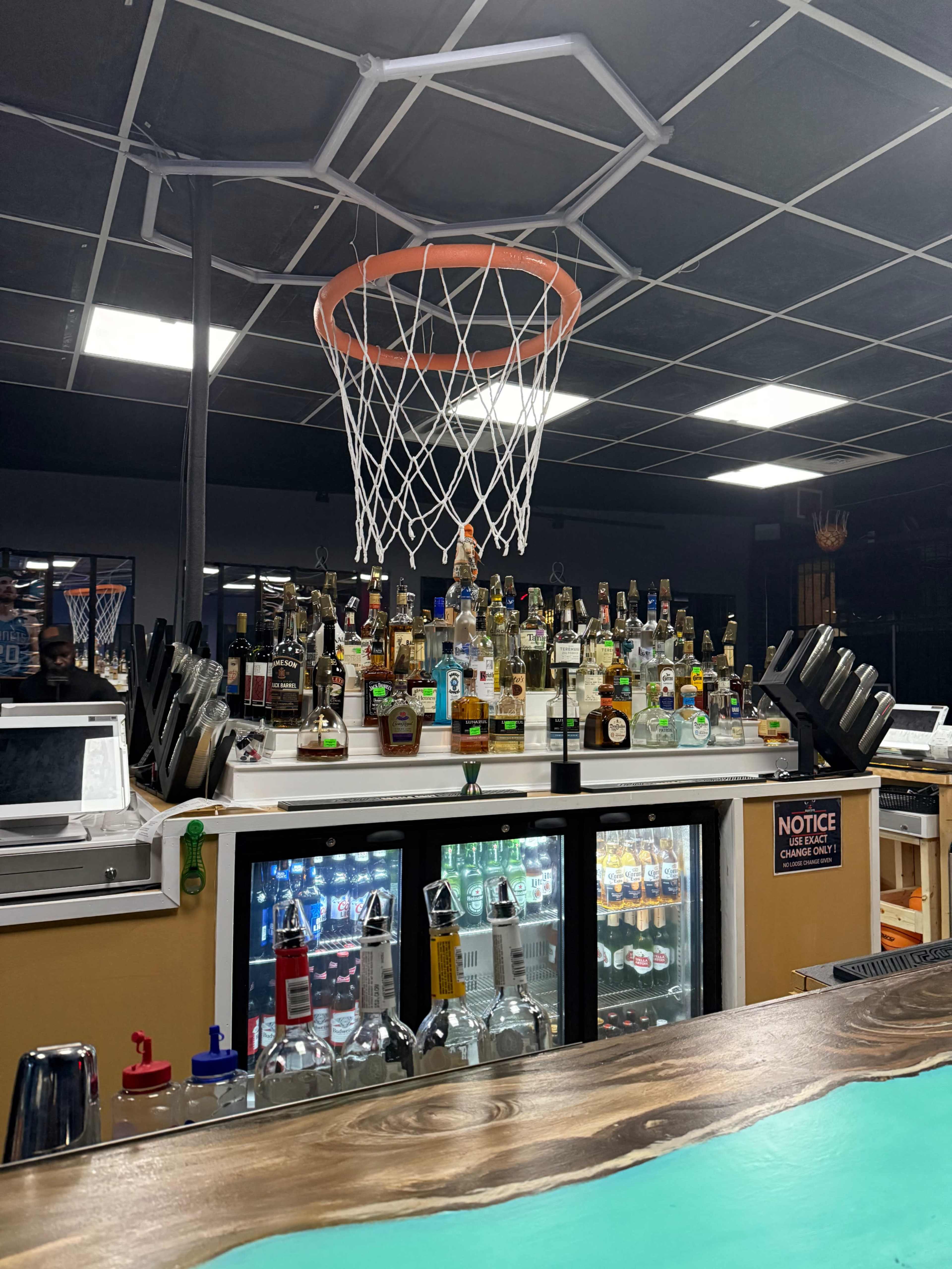 The image shows a bar with a basketball hoop above a shelf stocked with various bottles of alcoholic beverages.