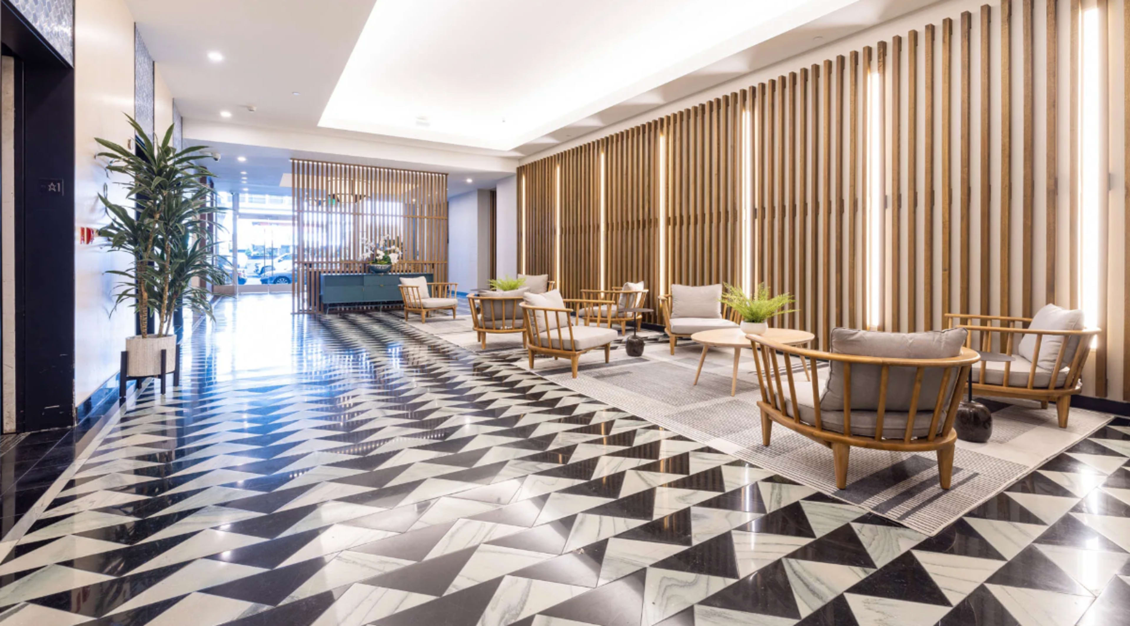 A modern lobby features geometric tile flooring, wooden wall paneling, and seating areas with plants.