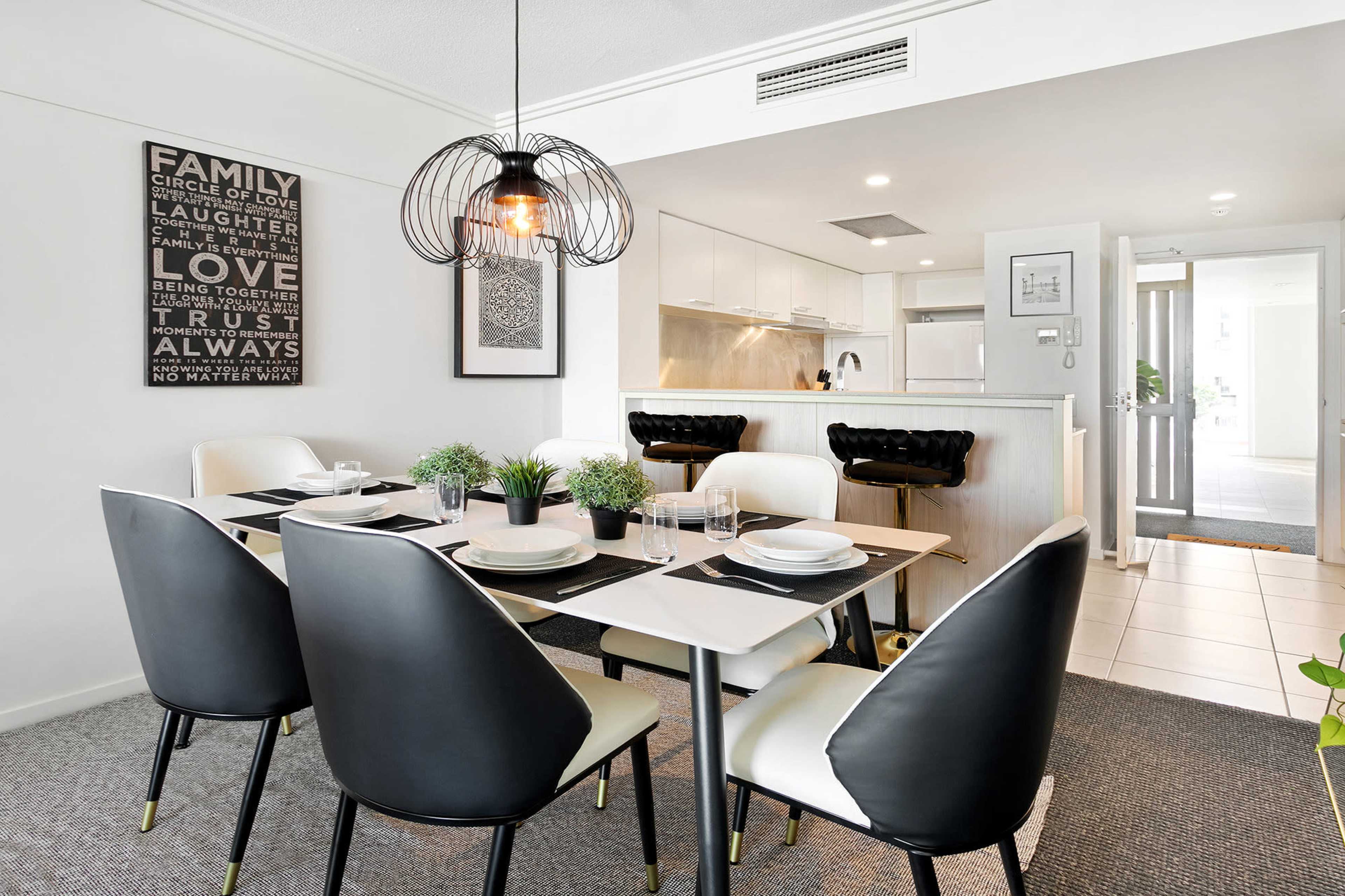 A dining area features a black and white table set with chairs, while a modern kitchen is visible in the background, complemented by a framed wall art piece.