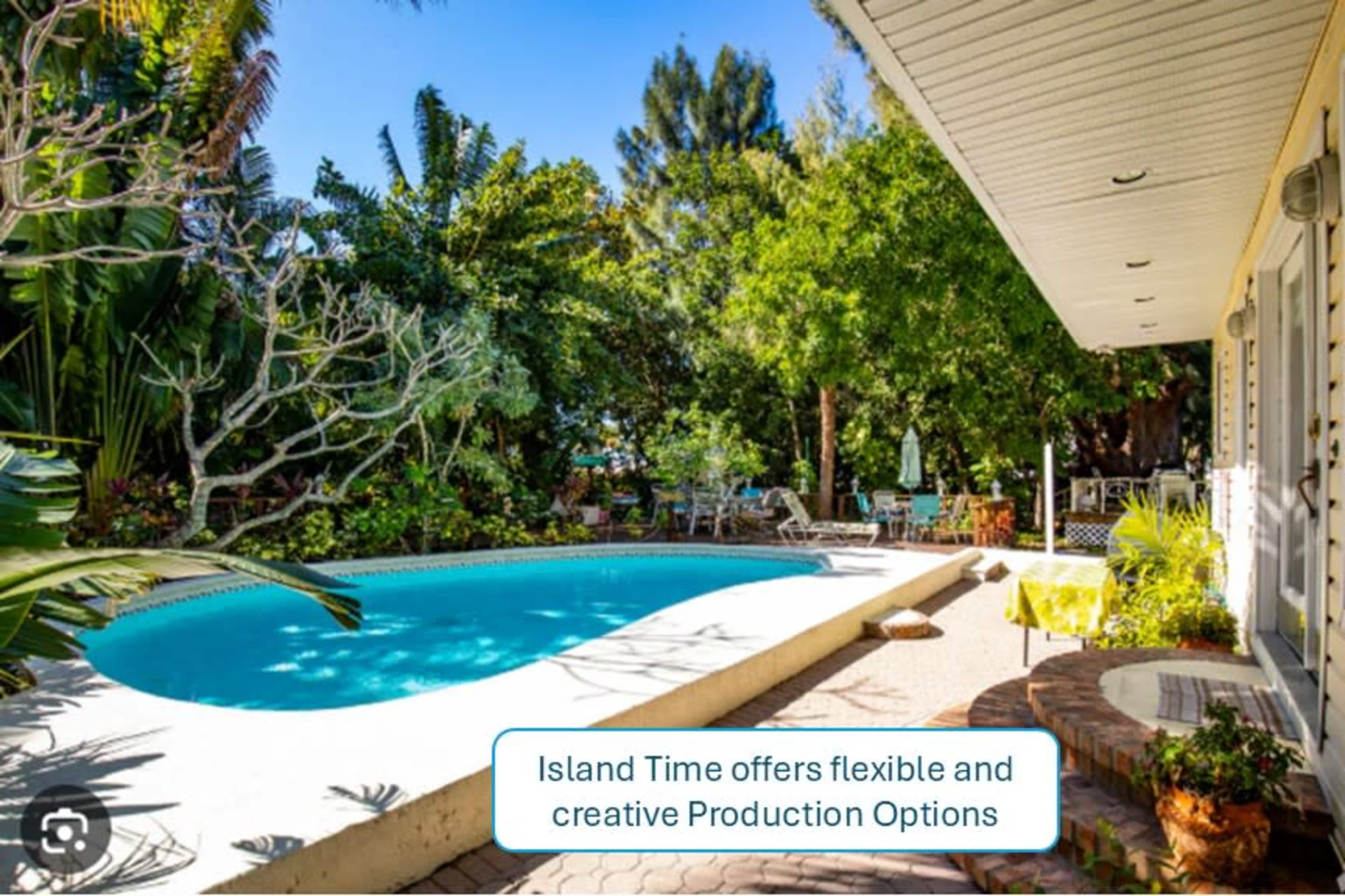A swimming pool surrounded by lush greenery and outdoor furniture is visible beside a house.