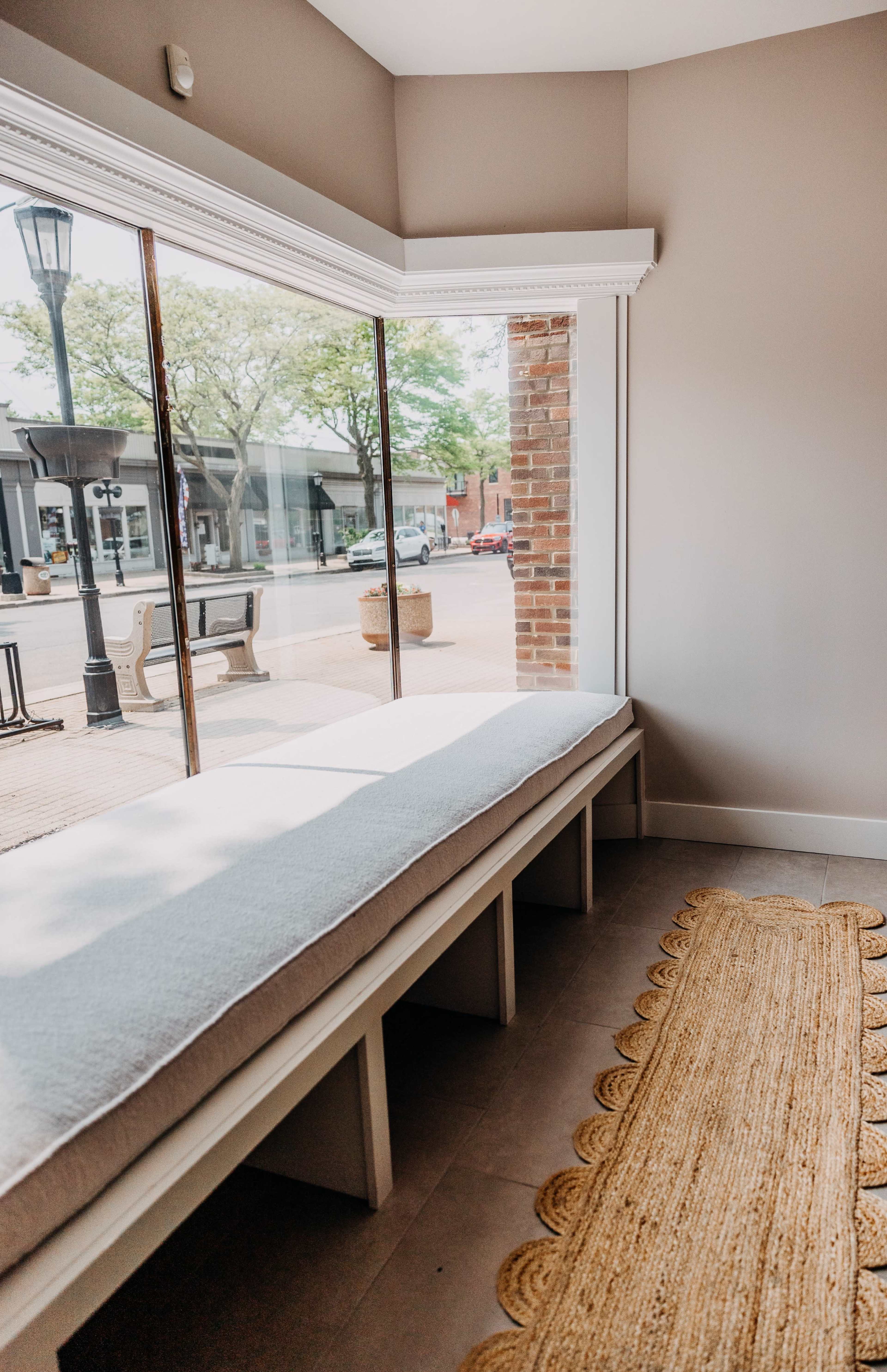 A cozy seating area with a long, cushioned bench by a large window and a woven rug on the floor.