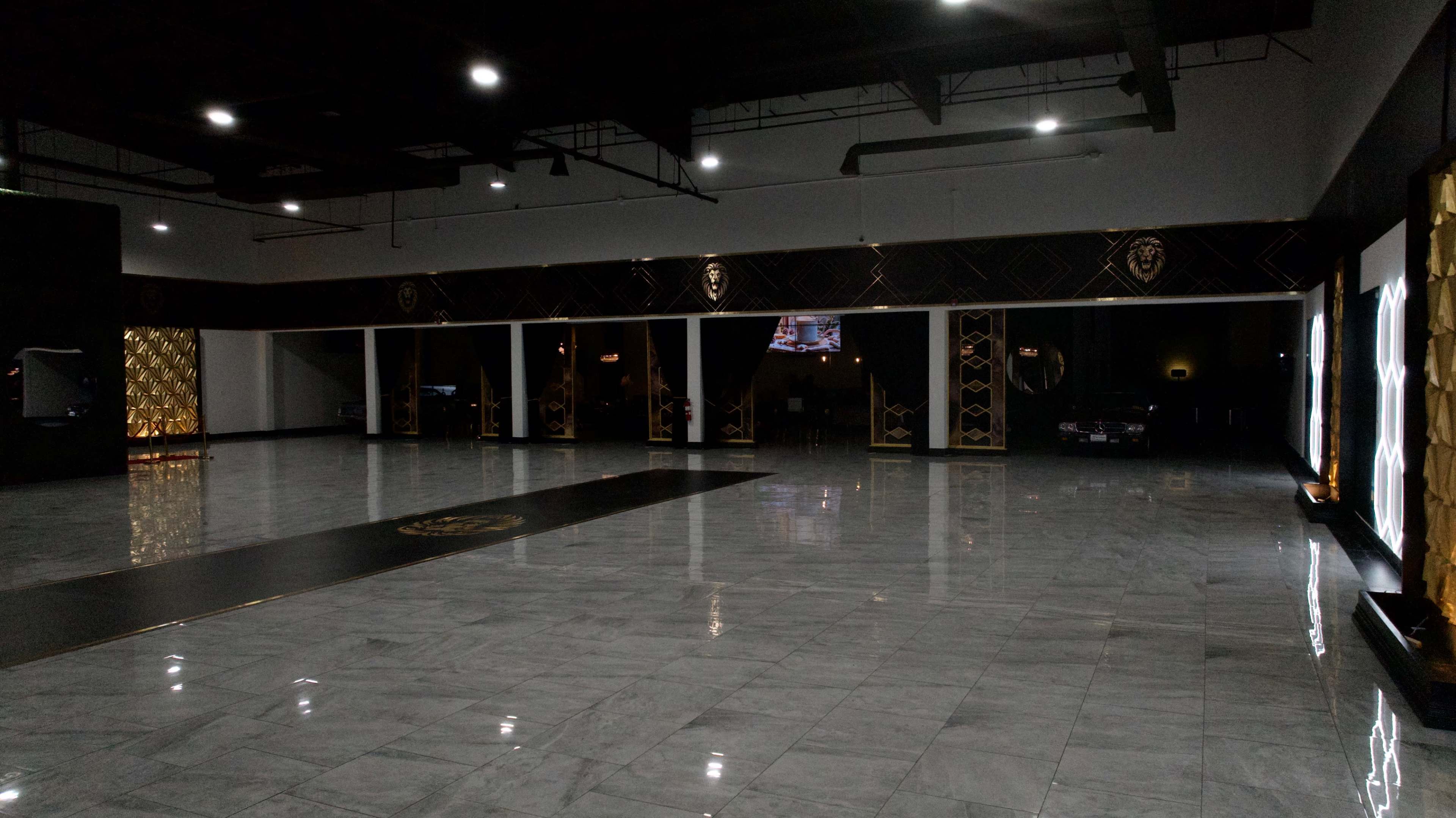 The image shows a large, empty indoor space with polished marble flooring and dark, elegant decor featuring gold accents.
