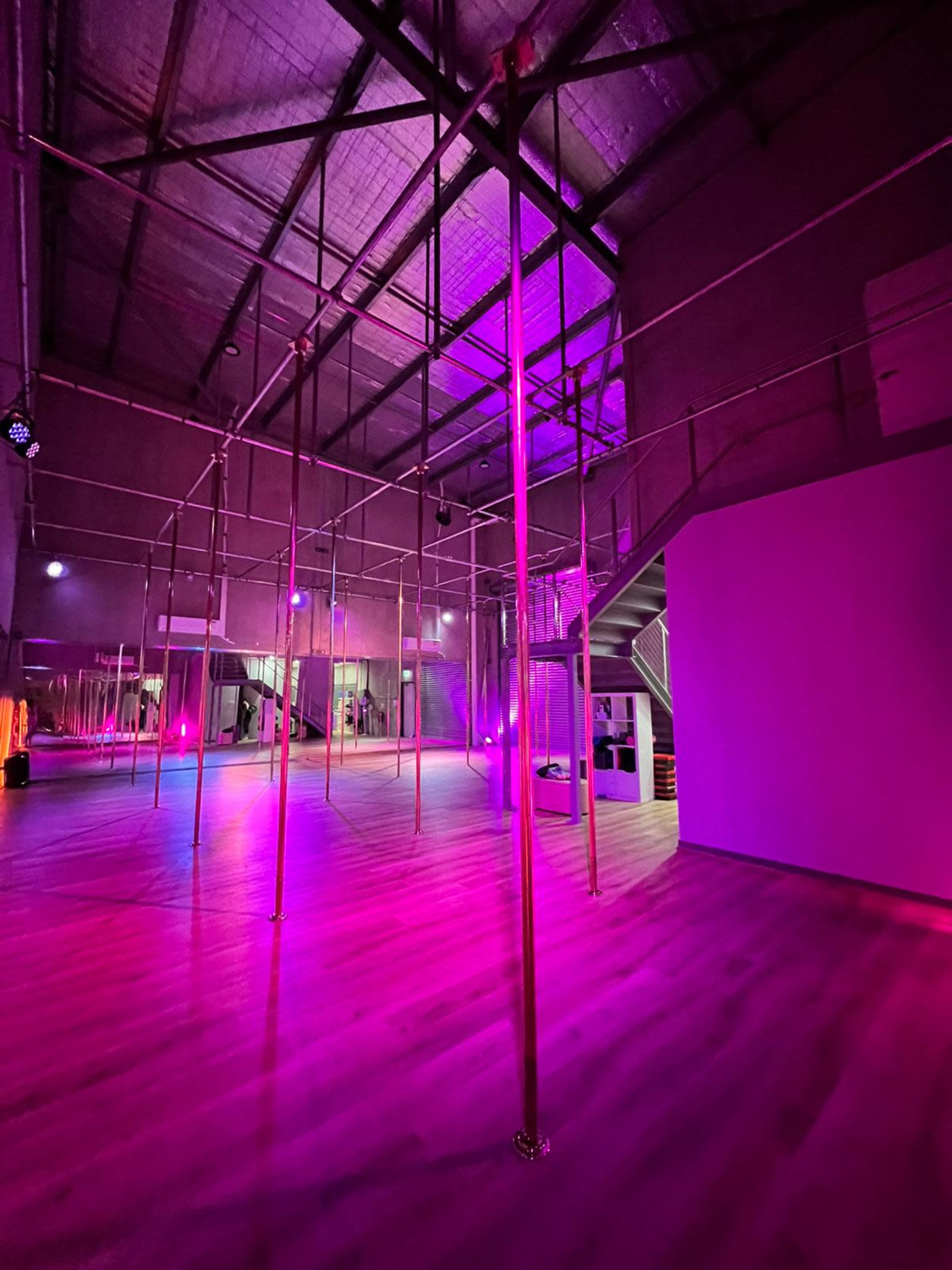 A spacious indoor area with framed poles and dim lighting in shades of pink and purple.