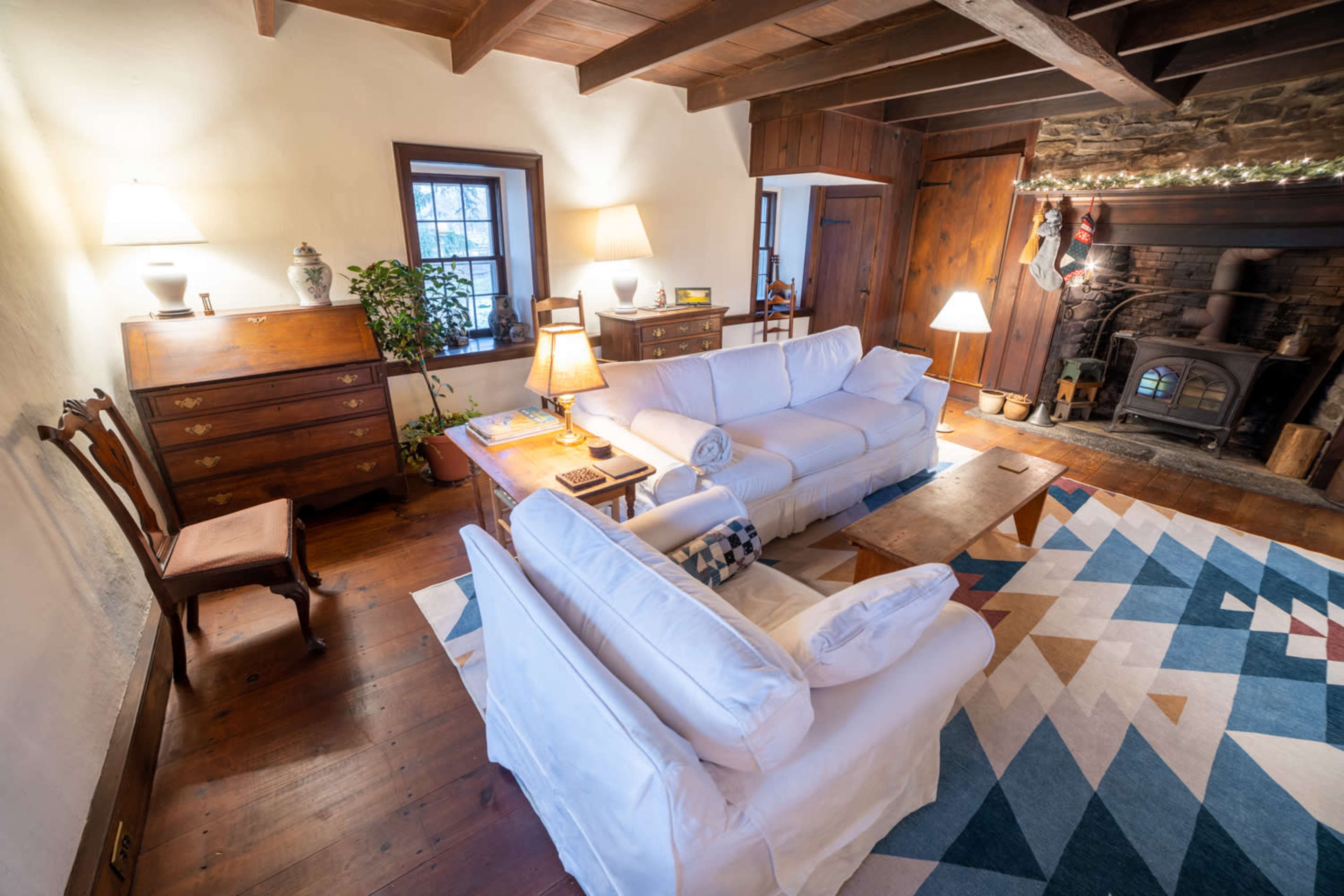The living room features two white sofas, a wooden coffee table, a patterned rug, and a stone fireplace with stockings above it.