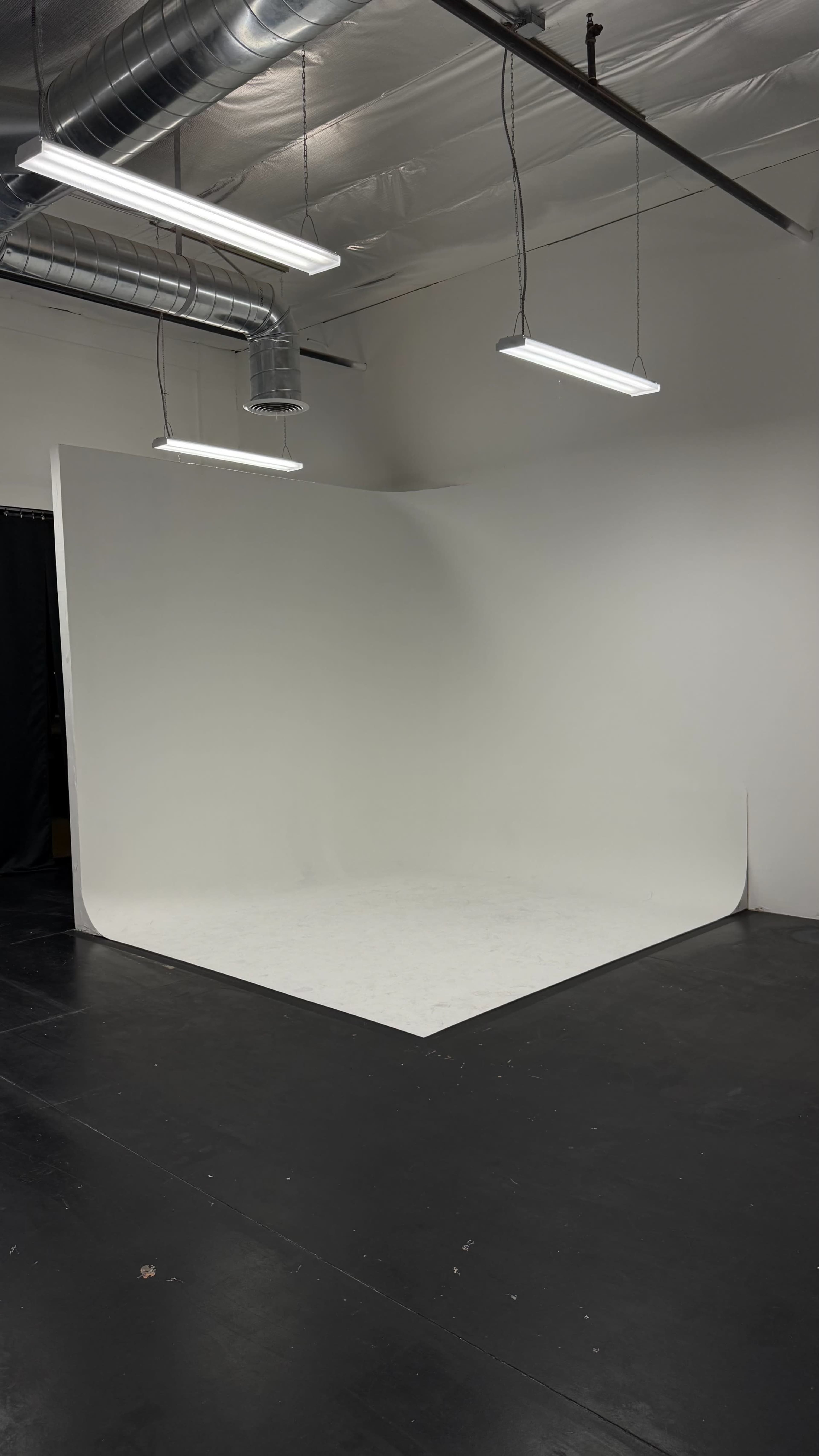 The image shows a minimalist photography studio featuring a large seamless white backdrop and a black floor.
