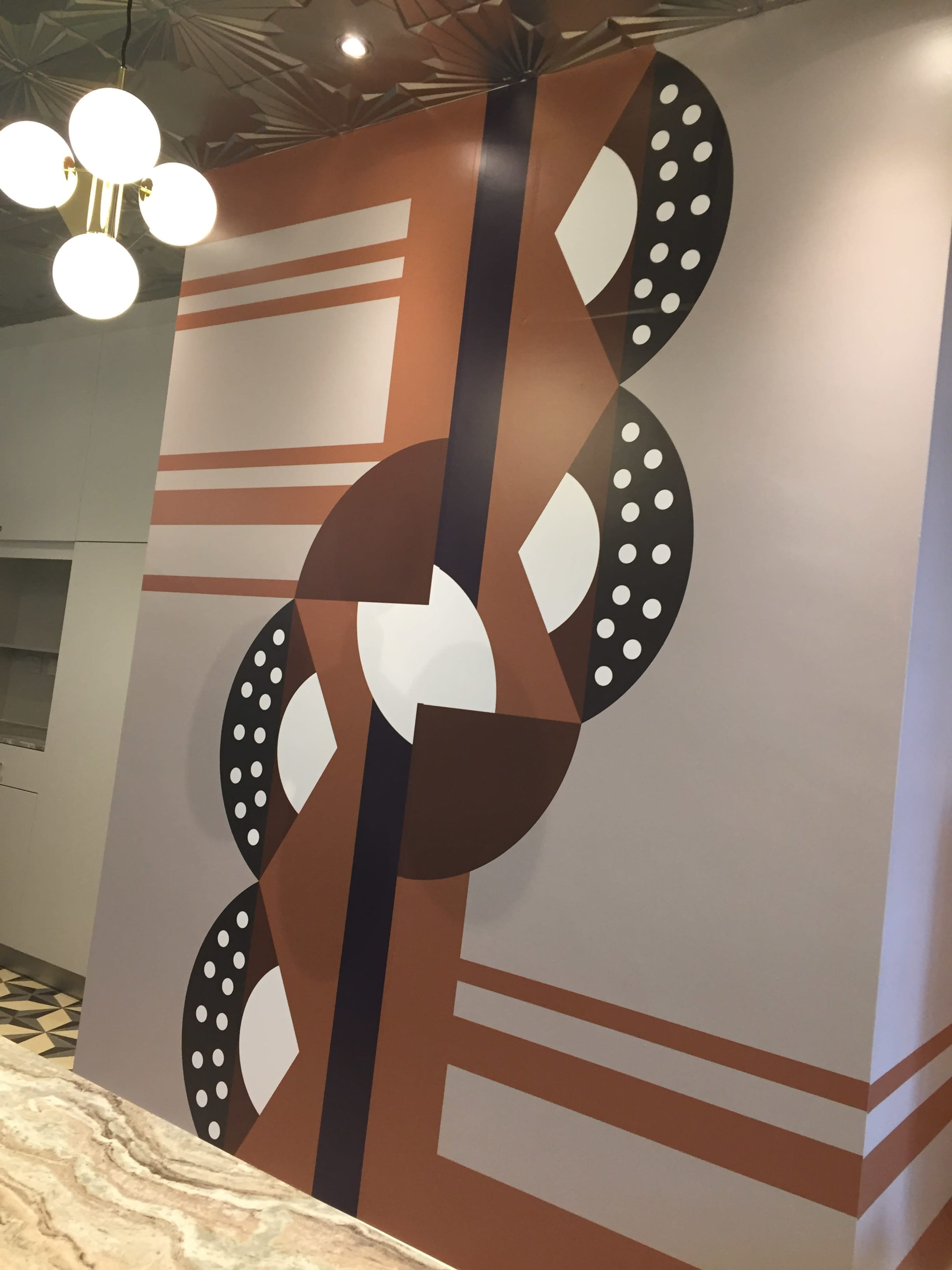 A large wall mural with geometric shapes, including circles and lines, arranged in a stylized pattern of brown, black, and white.