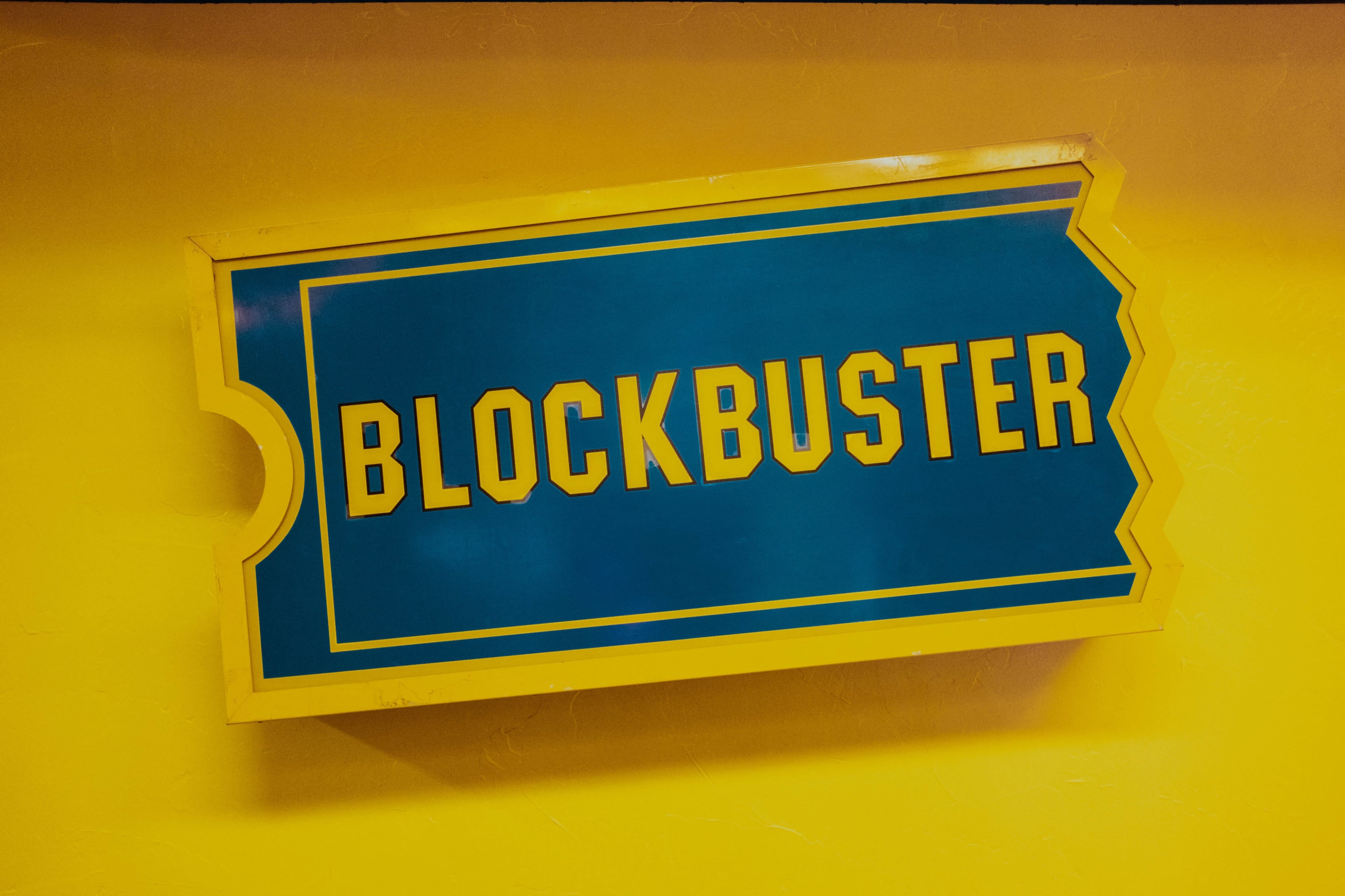 The image features a large, blue and yellow sign displaying the word "BLOCKBUSTER."