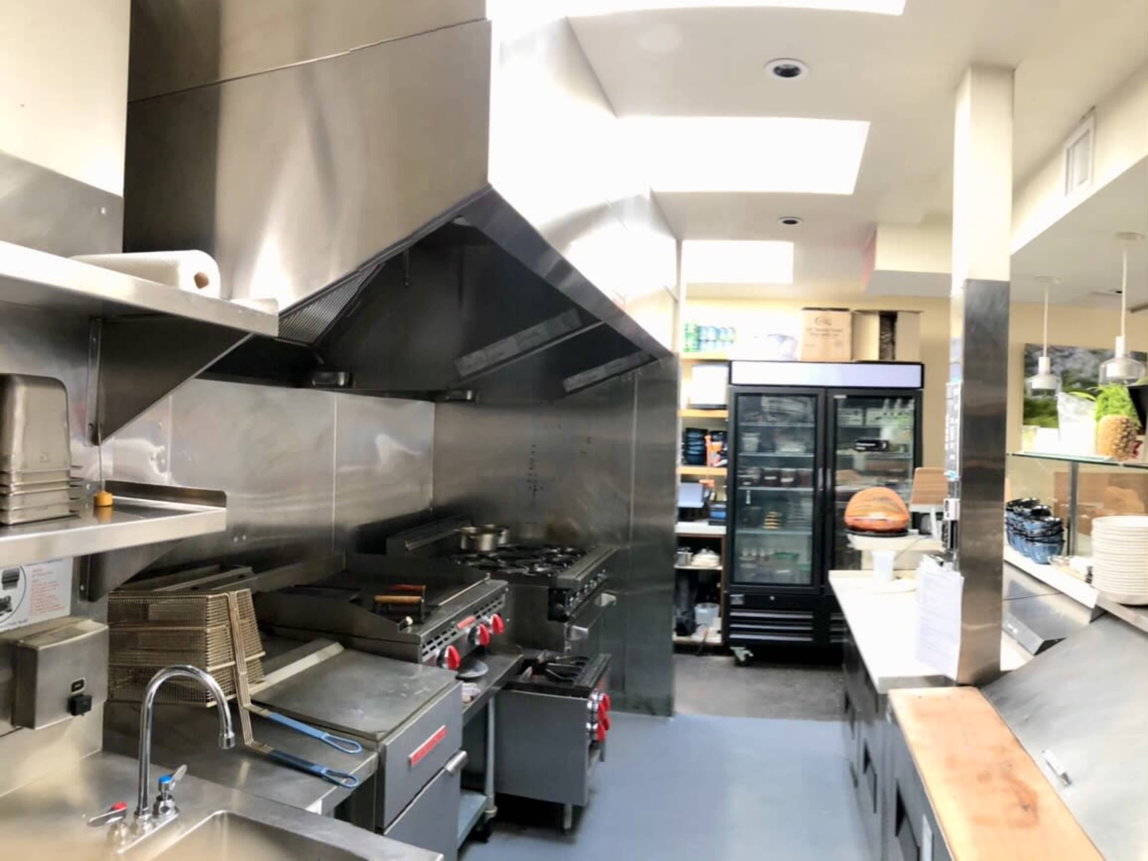 A stainless steel kitchen featuring industrial cooking equipment, a refrigerator, and a countertop with dishes.