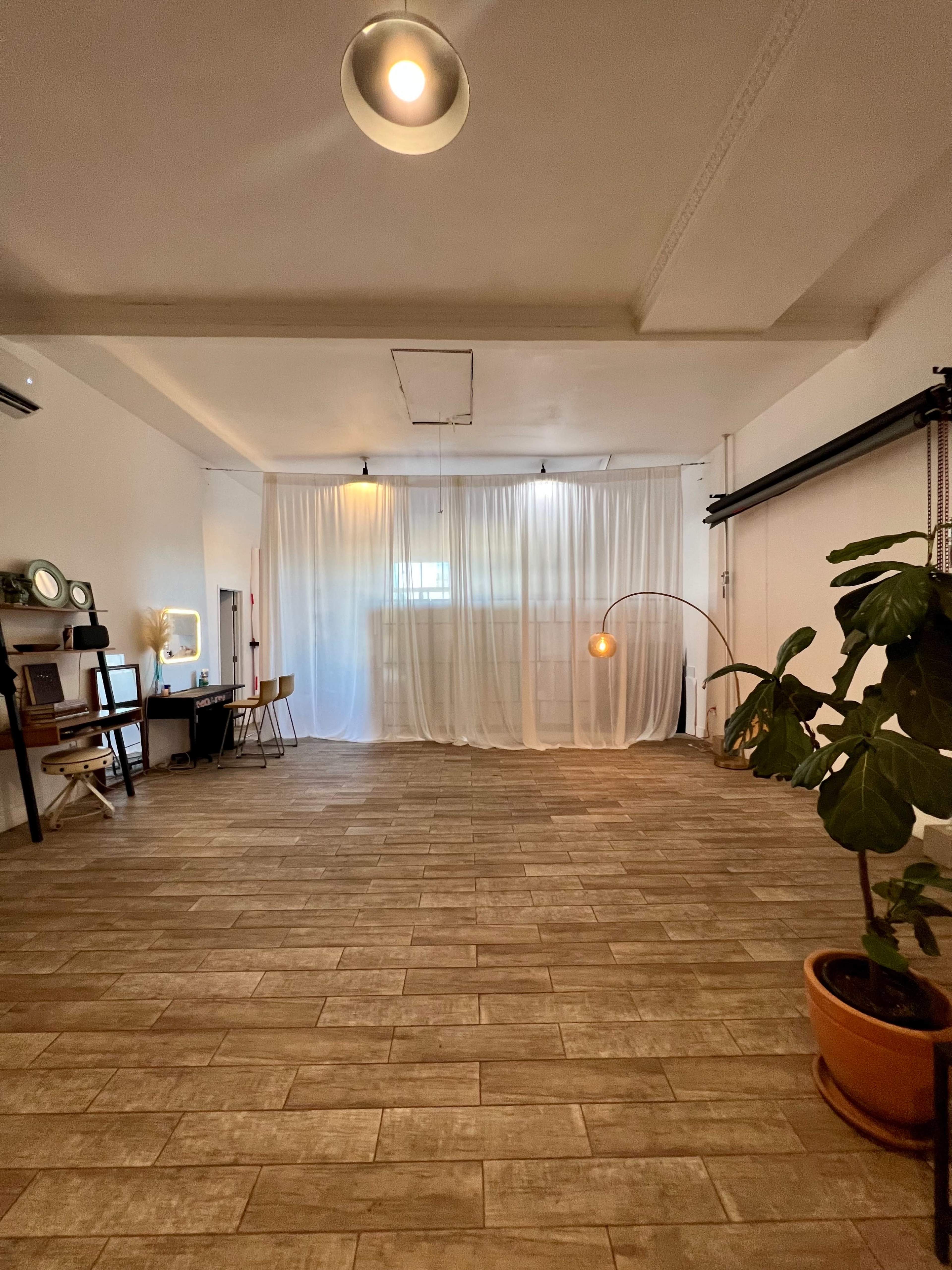 A spacious, well-lit room with tiled flooring, curtain dividers, a plant in a pot, and a mid-century floor lamp.