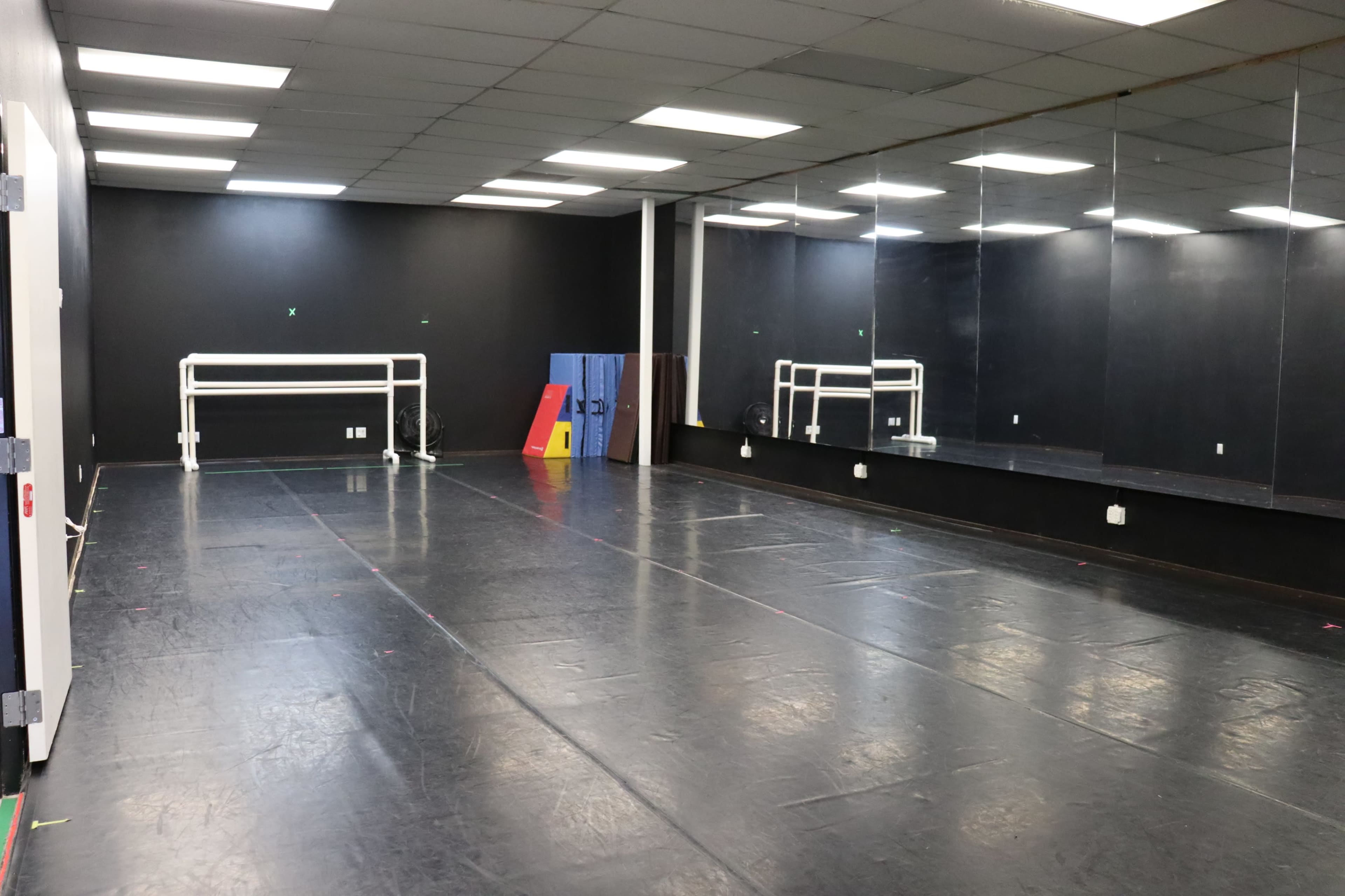The image shows a spacious dance studio with mirrored walls, a black floor, and a barres along one side.