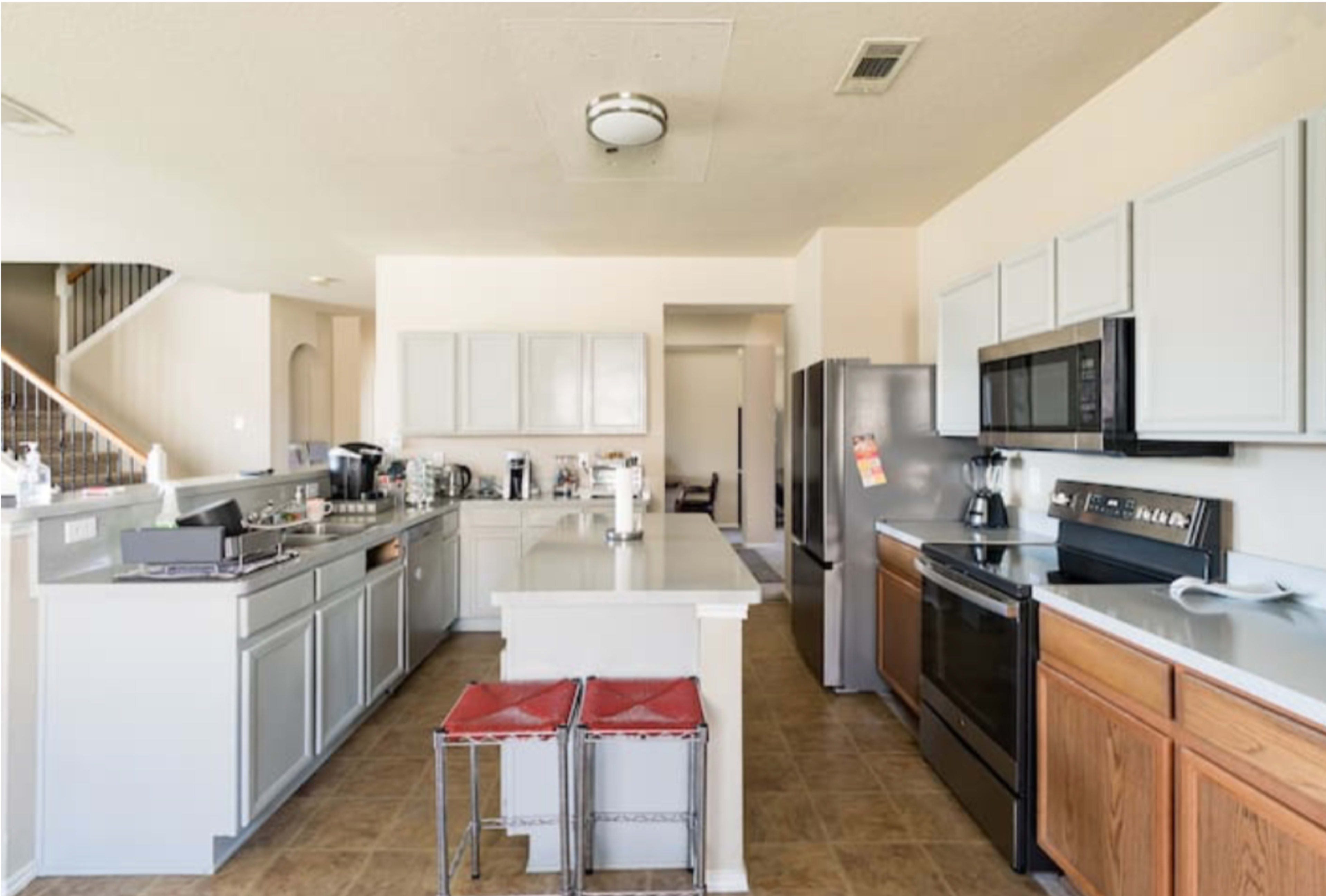 A spacious kitchen features gray cabinets, stainless steel appliances, and a central island with two red stools.