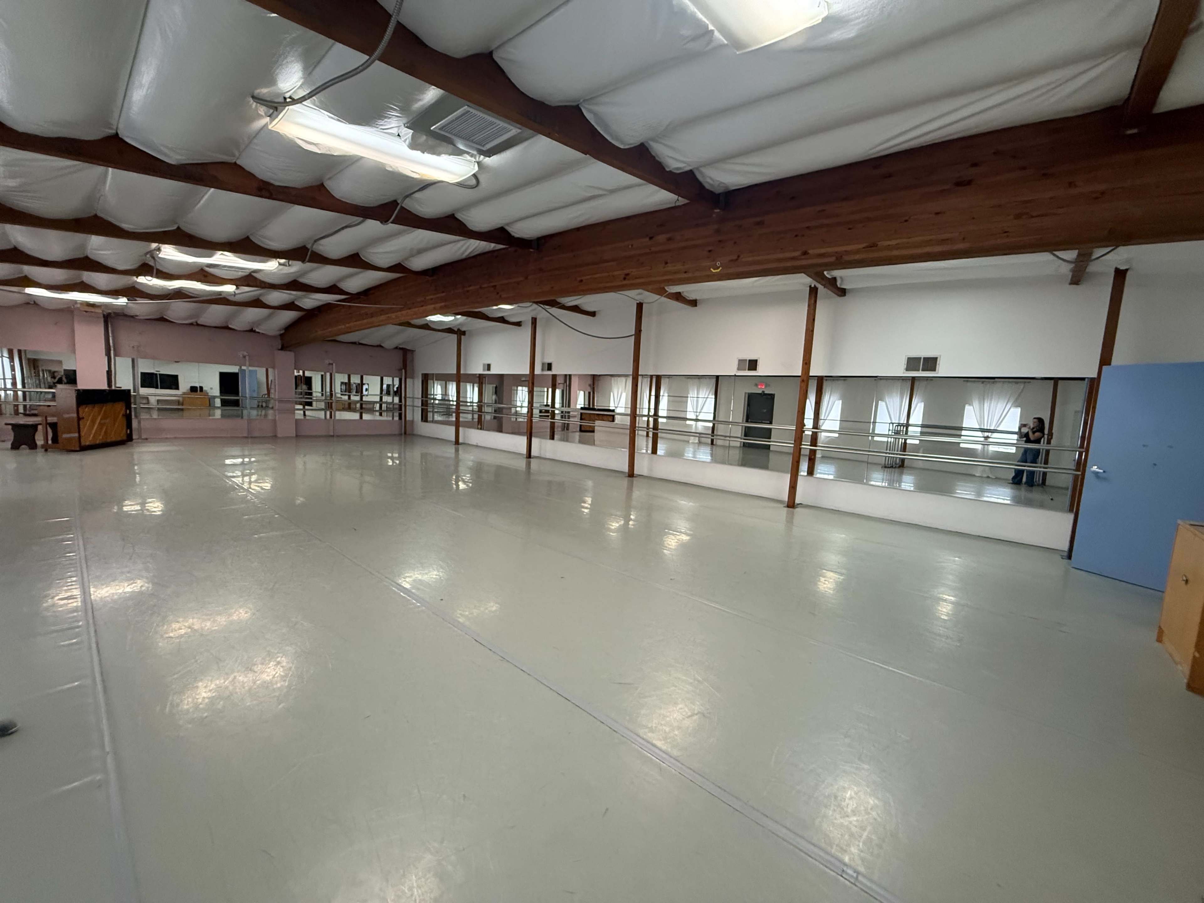 An empty dance studio features mirrored walls and a polished floor under a wooden beam ceiling.