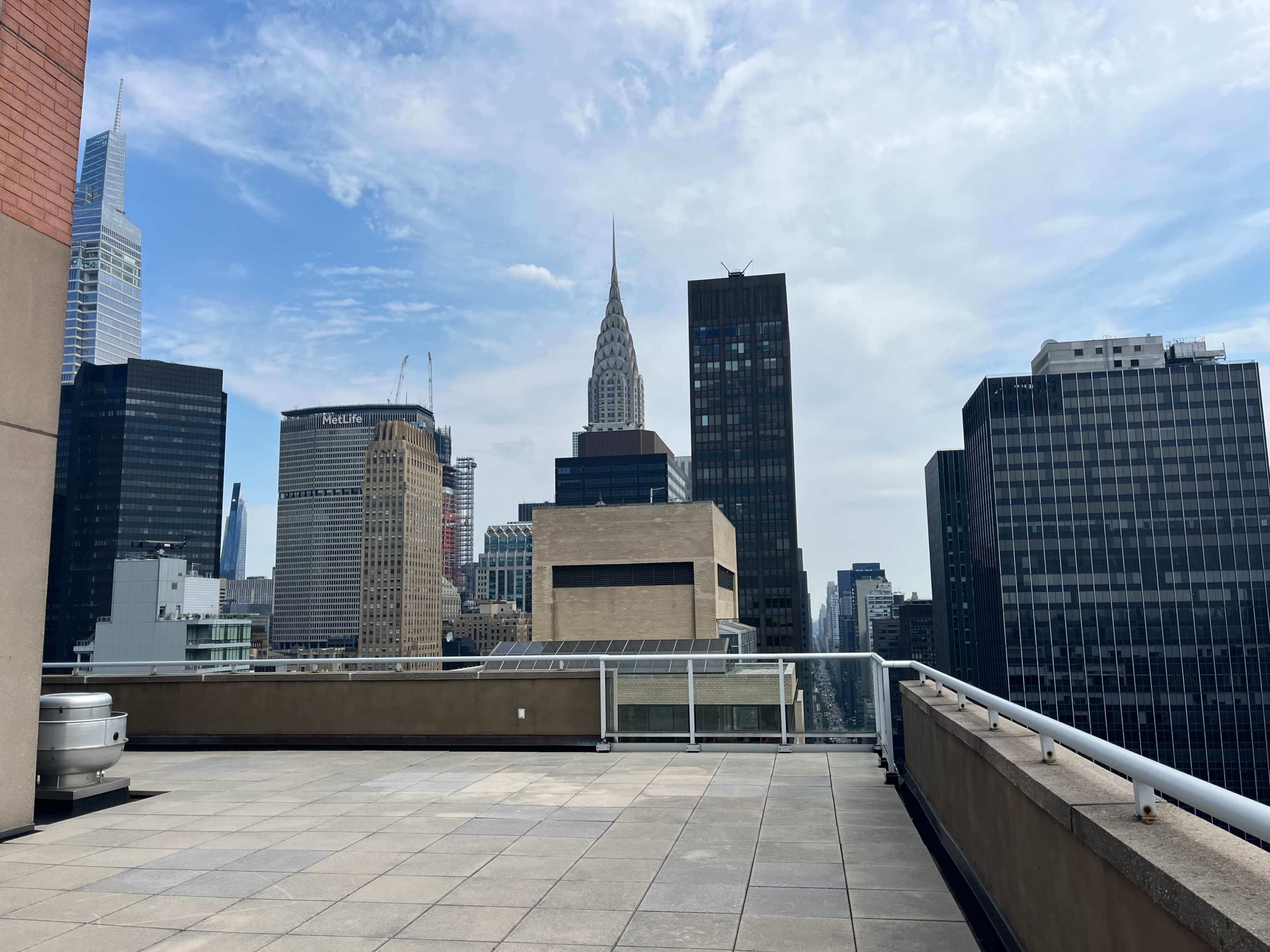 The image shows a rooftop view of skyscrapers in New York City, featuring the iconic Chrysler Building in the background.