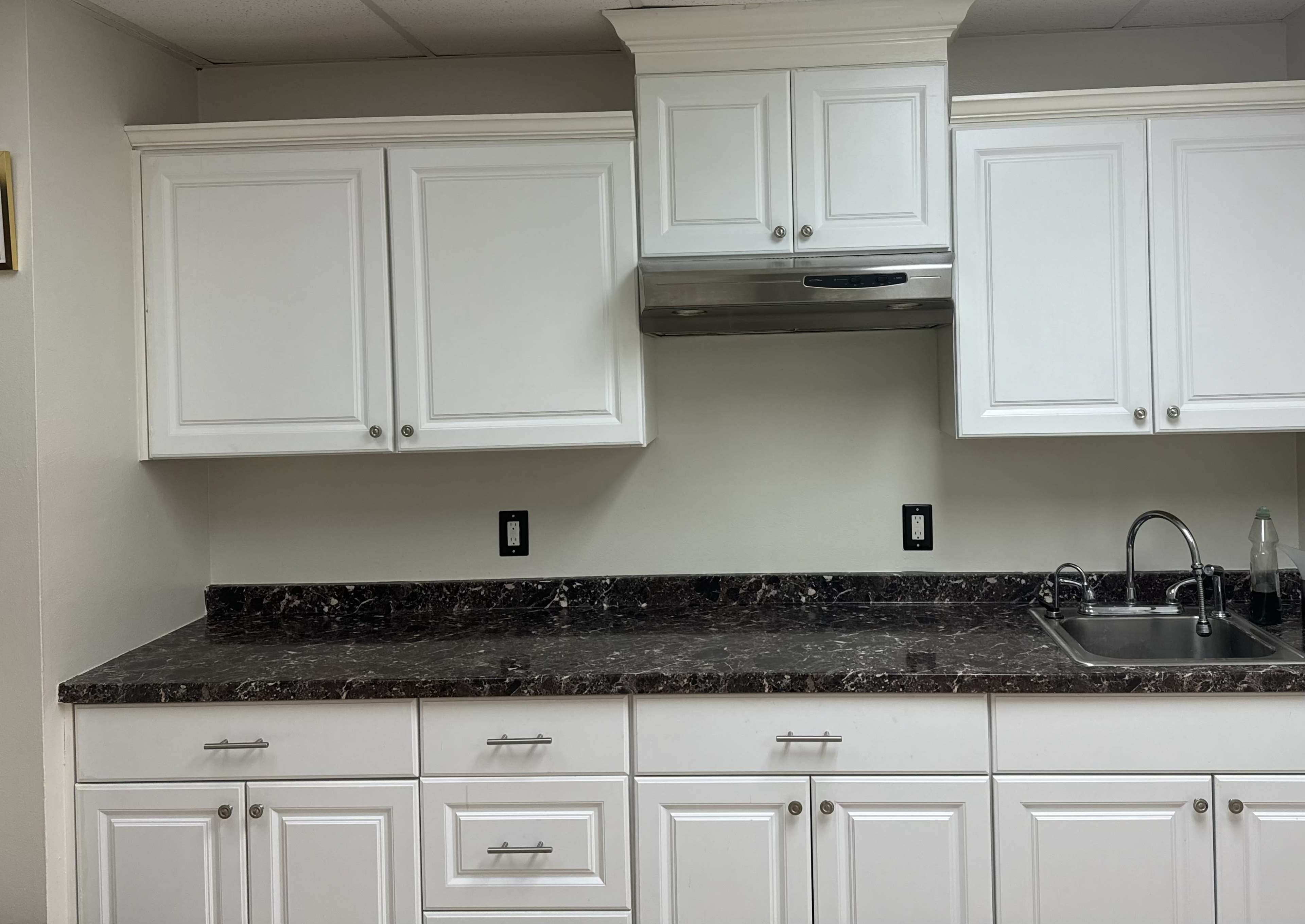 A kitchen with white cabinetry and a dark countertop, featuring a sink on the right and a ventilation hood above.
