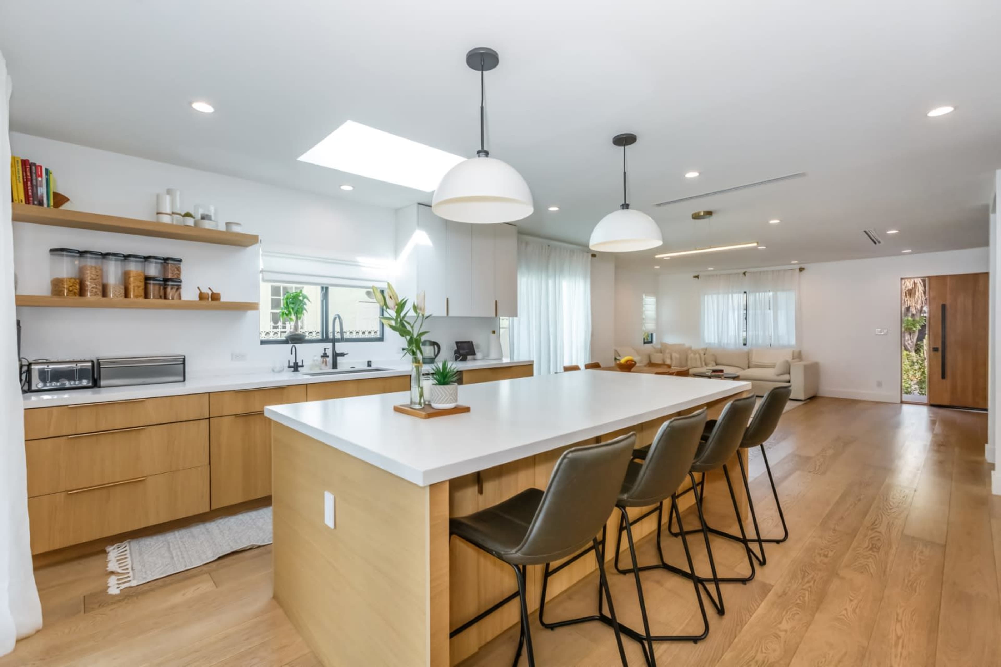 A modern kitchen features a large island with seating, sleek cabinetry, and ample natural light from overhead skylights.
