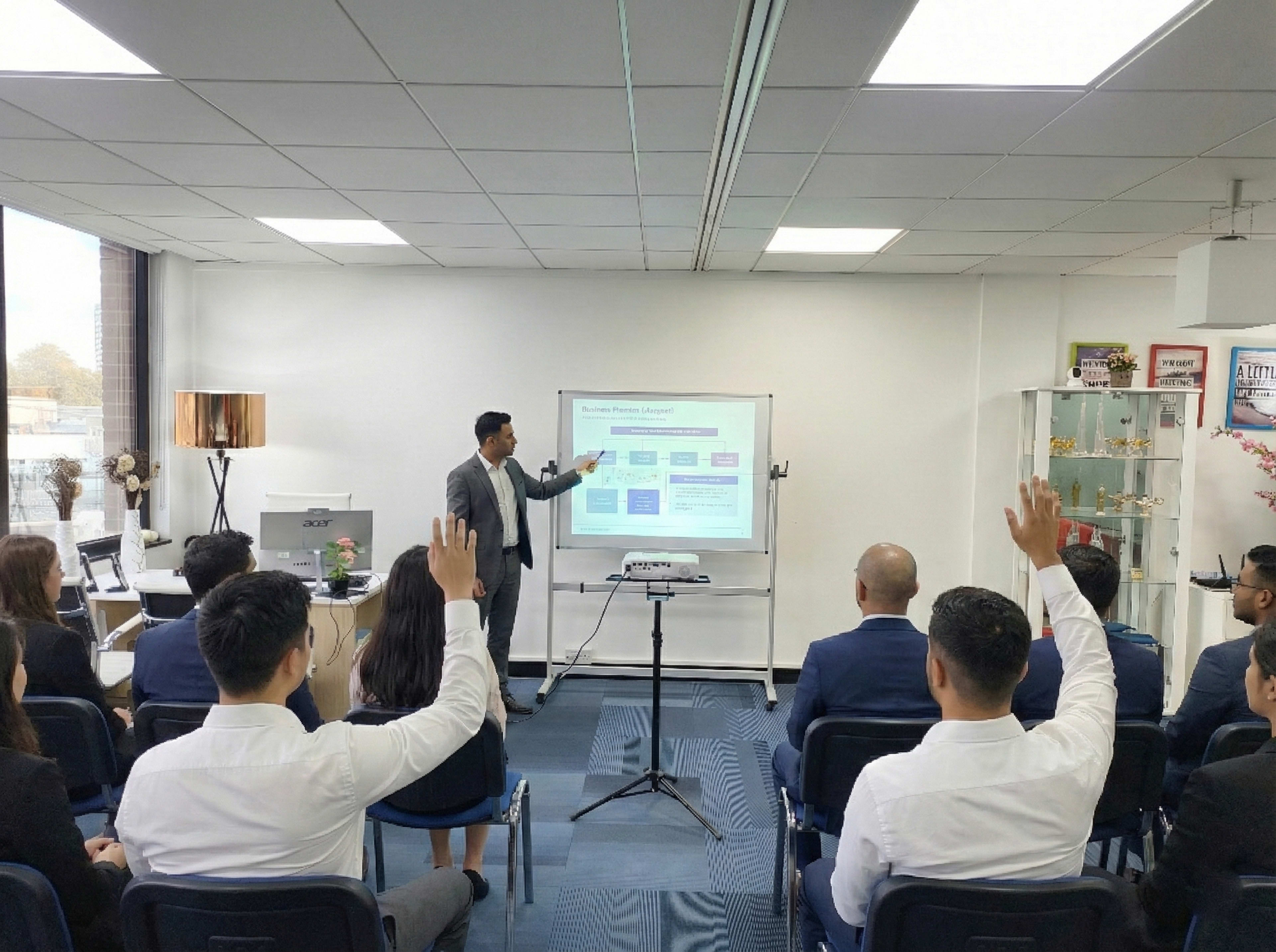 A presenter gestures towards a screen while an audience raises their hands for questions in a modern office setting.