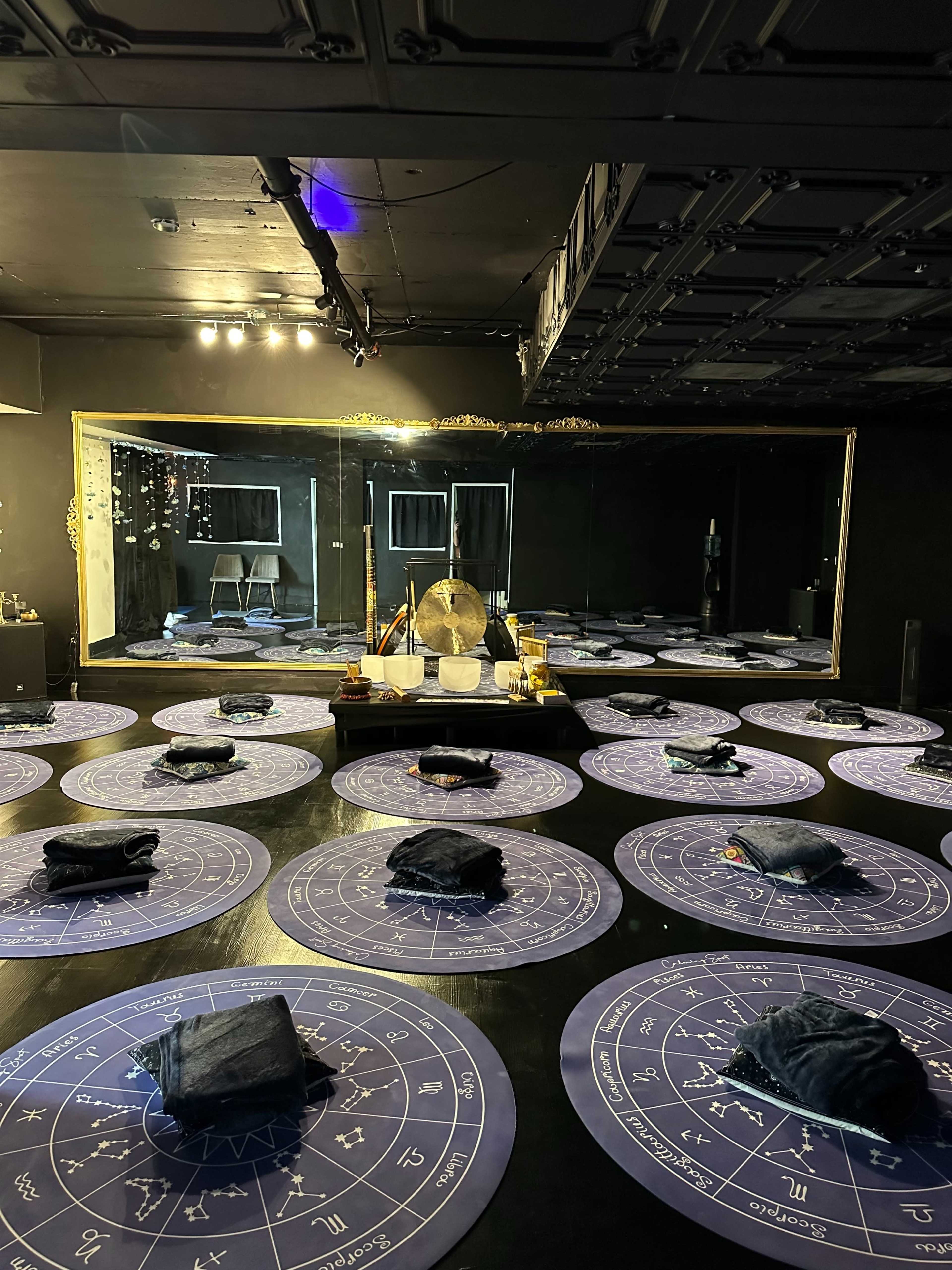 A dimly lit room with circular mats arranged on the floor, a large mirror at the back, and various sound instruments set up in the center.