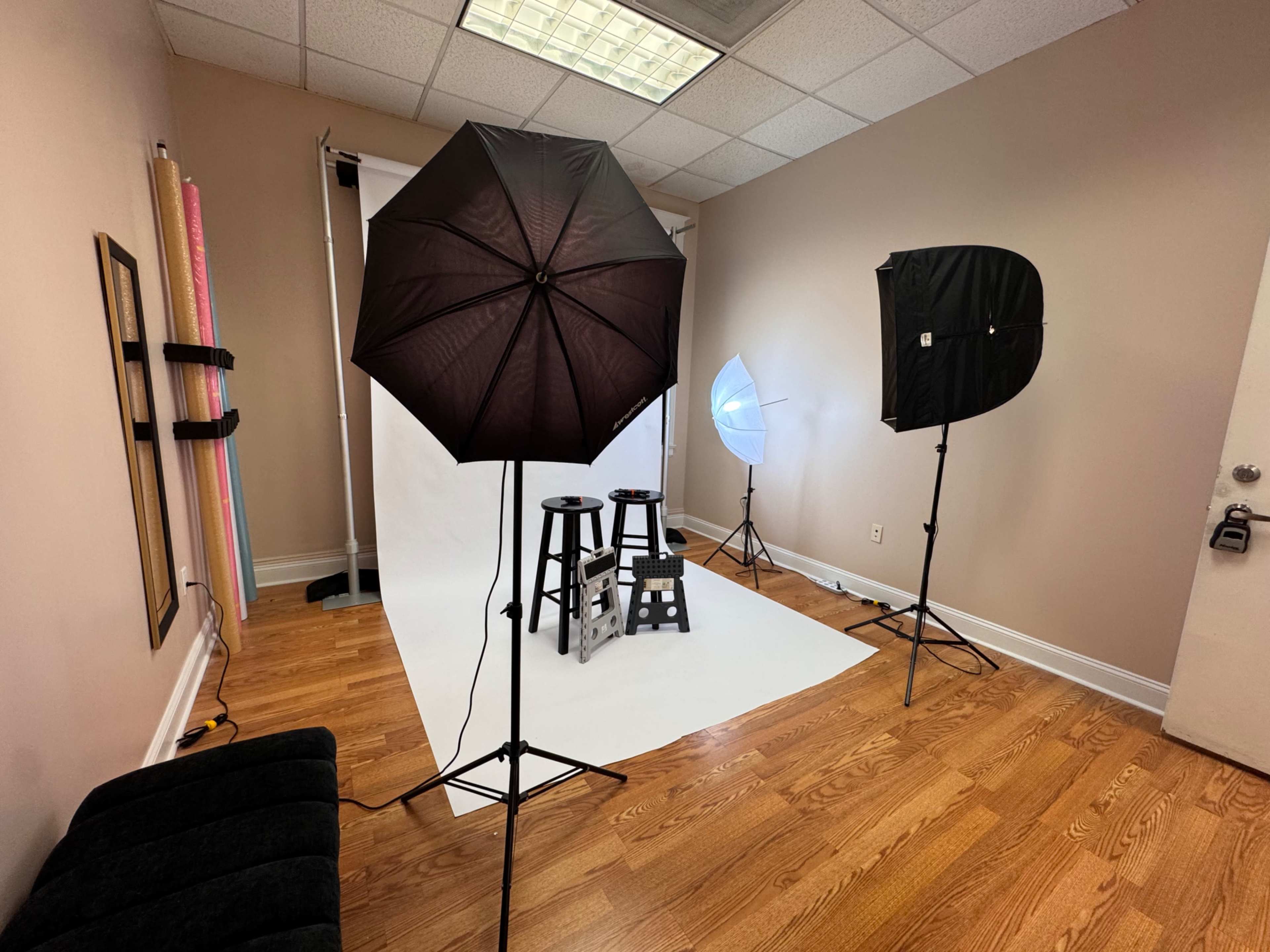 The image shows a photography studio setup with two stools, a backdrop, and lighting equipment positioned around the space.
