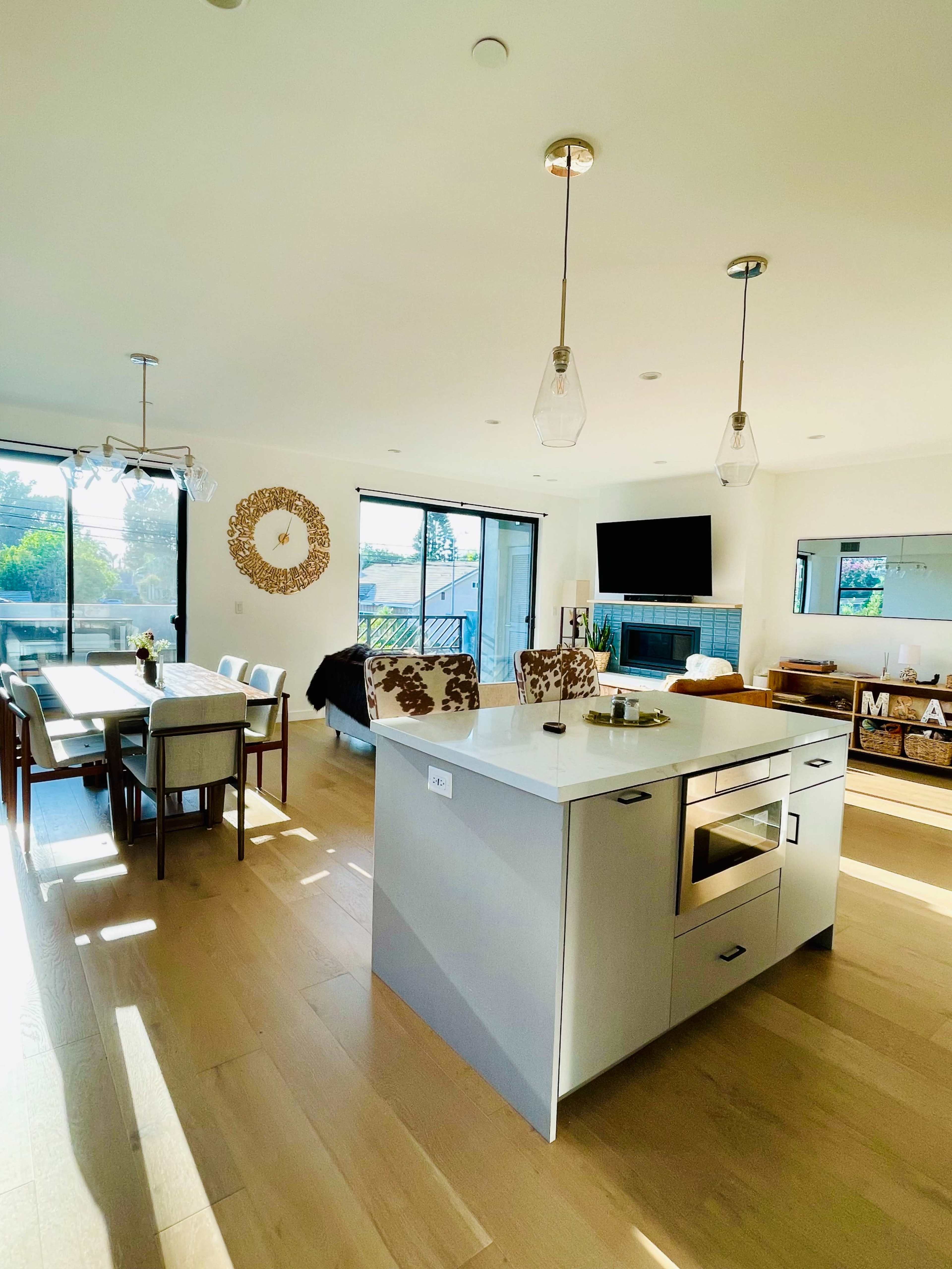 A modern kitchen and dining area features an island with seating, a large dining table, and large windows that provide natural light.