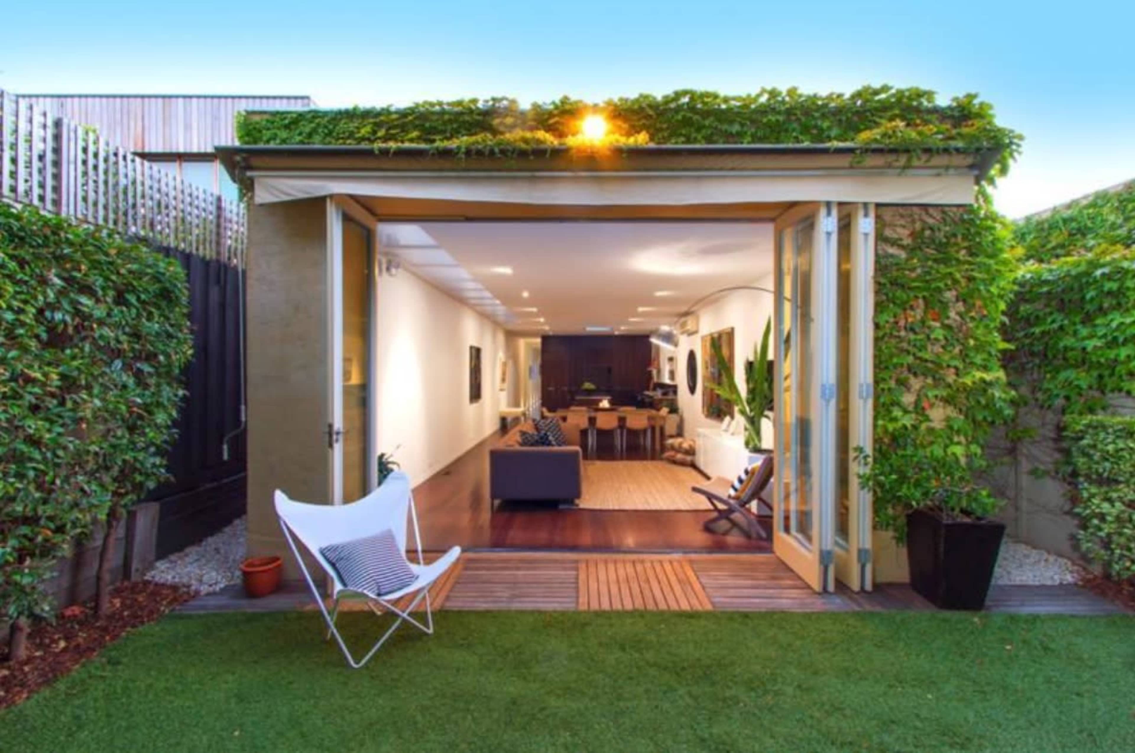 A modern open-concept living space opens to a landscaped garden, featuring large glass doors and greenery along the exterior.