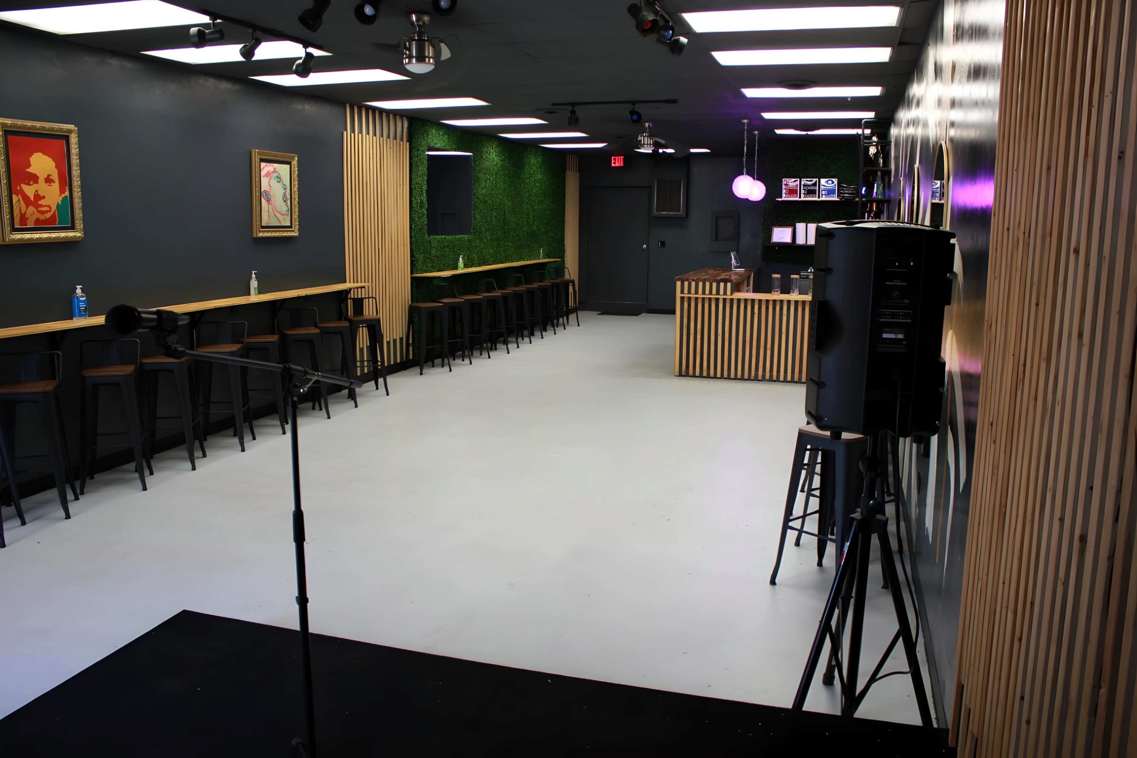 An empty indoor room featuring a bar area, high stools along a long counter, and microphone equipment set up for an event.