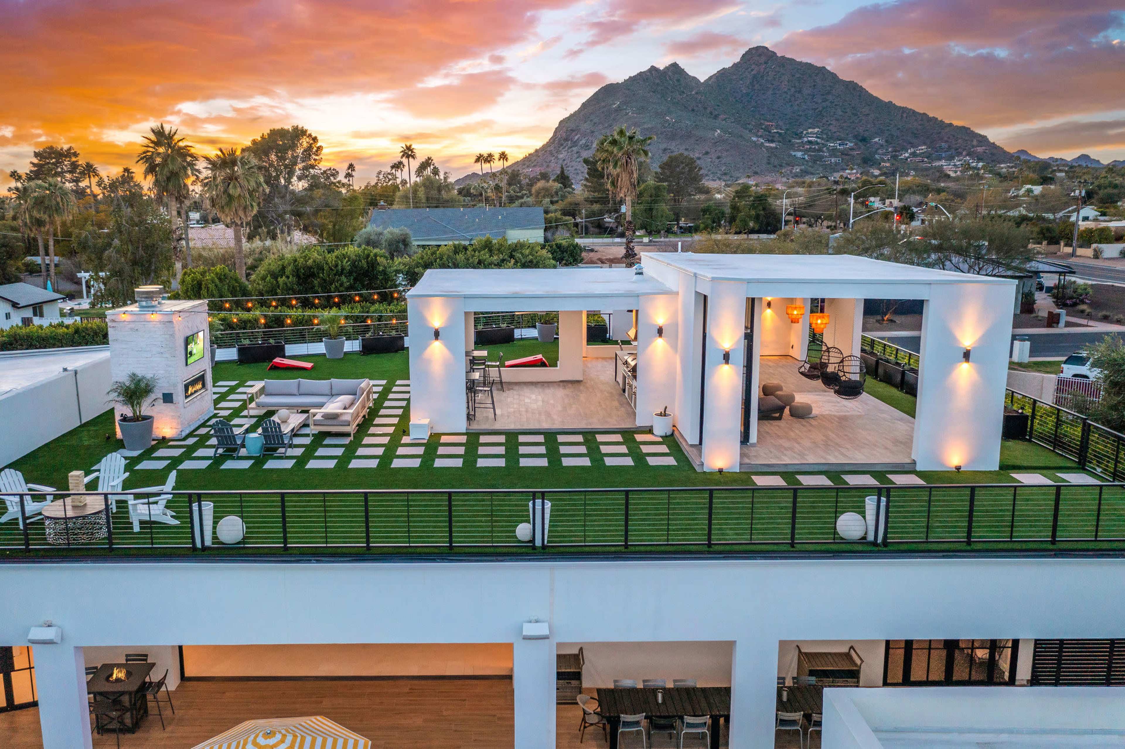 A rooftop terrace with landscaped grass, seating areas, and views of a mountainous landscape at sunset.