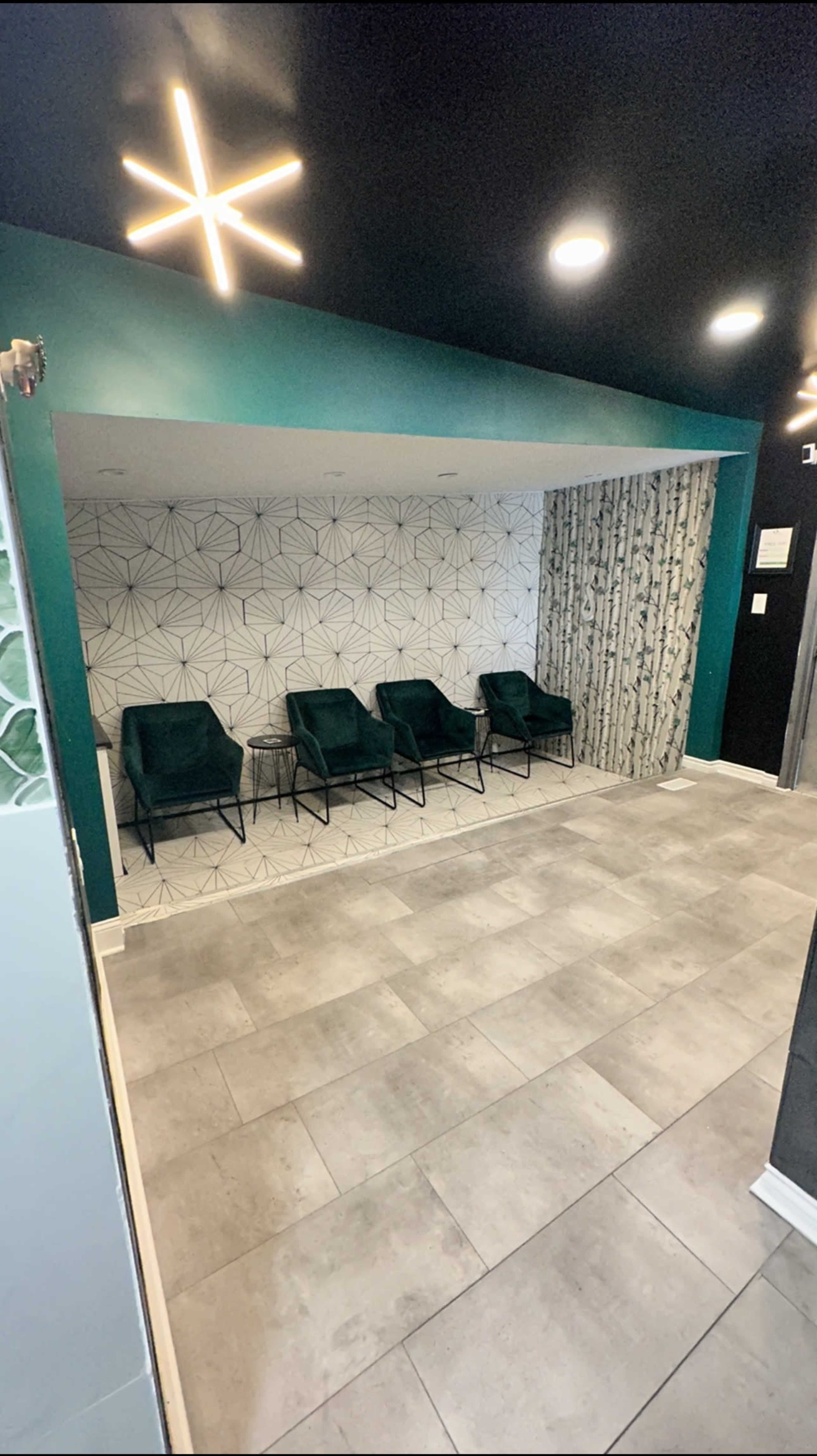 A waiting area with four green chairs against a geometric-patterned wall and a decorative curtain.