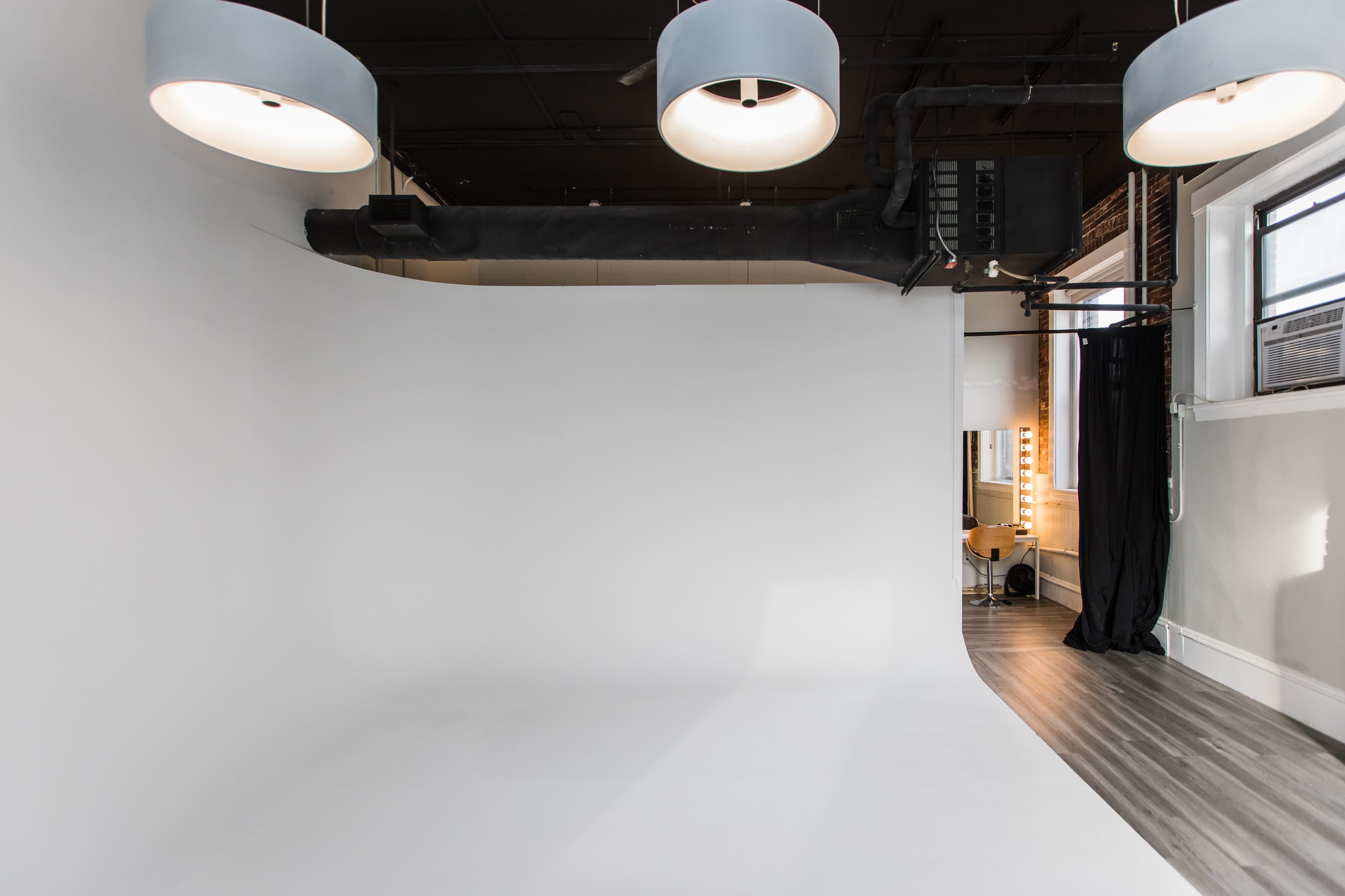 A spacious photo studio with a white backdrop, soft lighting fixtures, and wooden flooring.