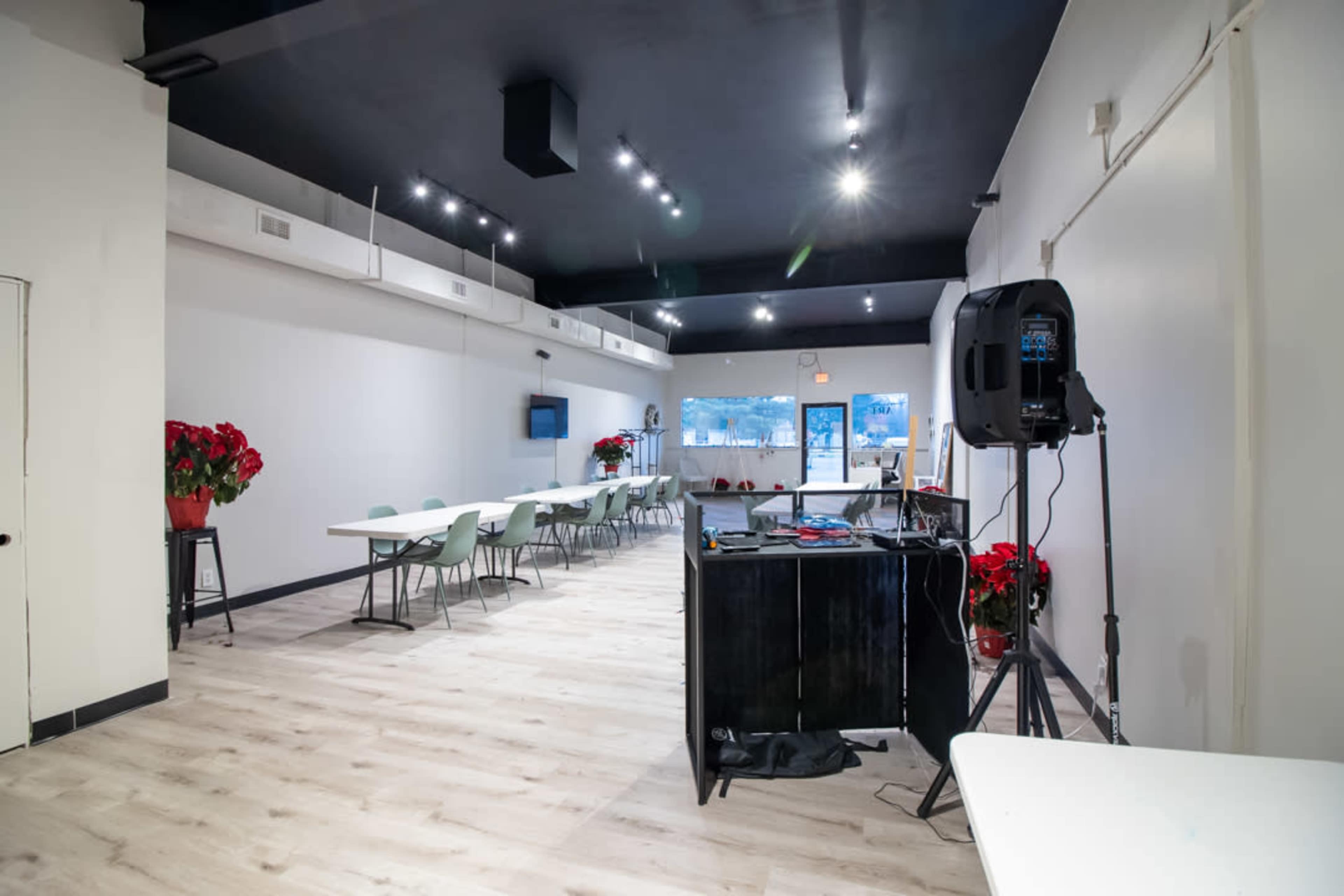 A spacious interior of a venue featuring several tables and chairs, with a microphone setup and a view of the entrance illuminated by overhead lighting.