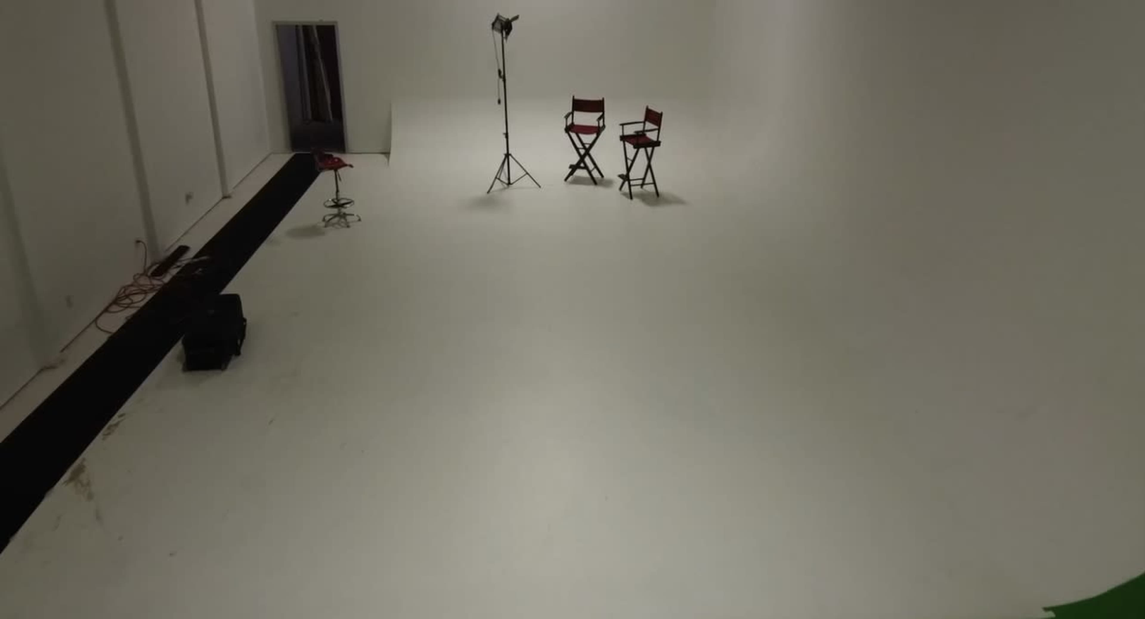The image shows a sparse photography studio with a white floor, two red chairs, a light stand, and a black mat on one side.