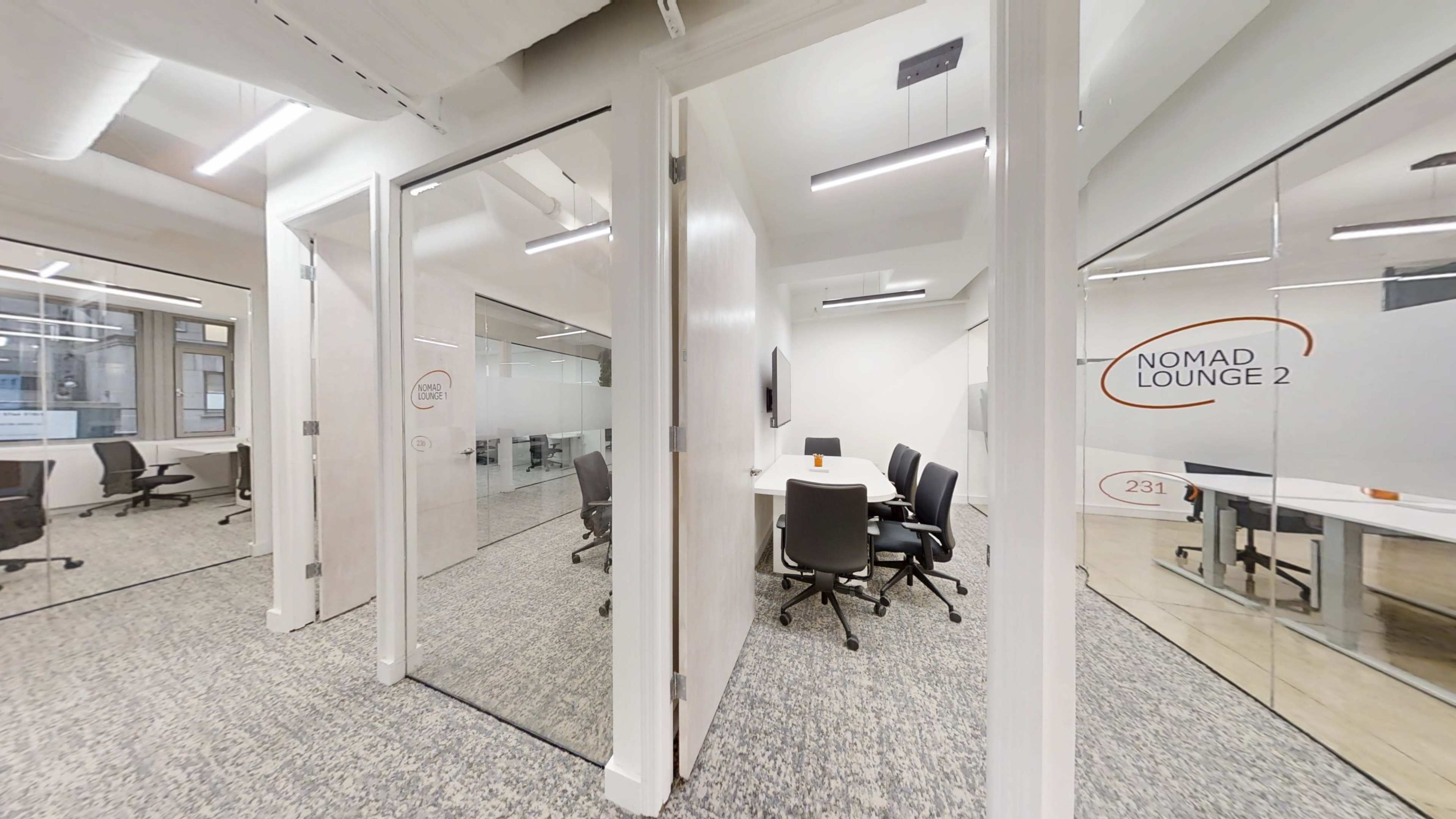 The image shows a modern office space featuring several glass-walled meeting rooms, each equipped with a table and chairs, in a well-lit environment.