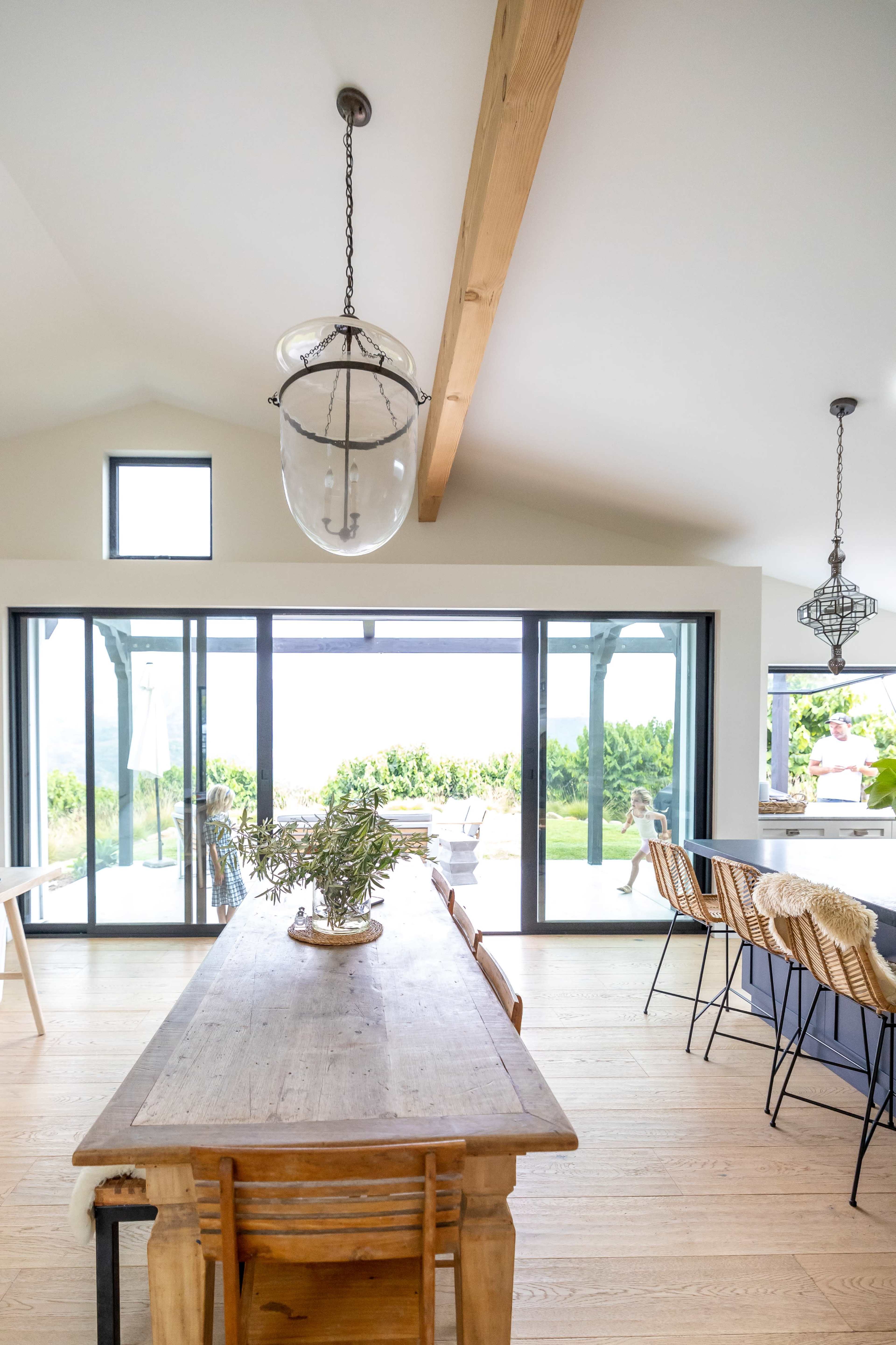 A spacious dining area features a long wooden table surrounded by chairs, with large glass doors opening to an outdoor view.