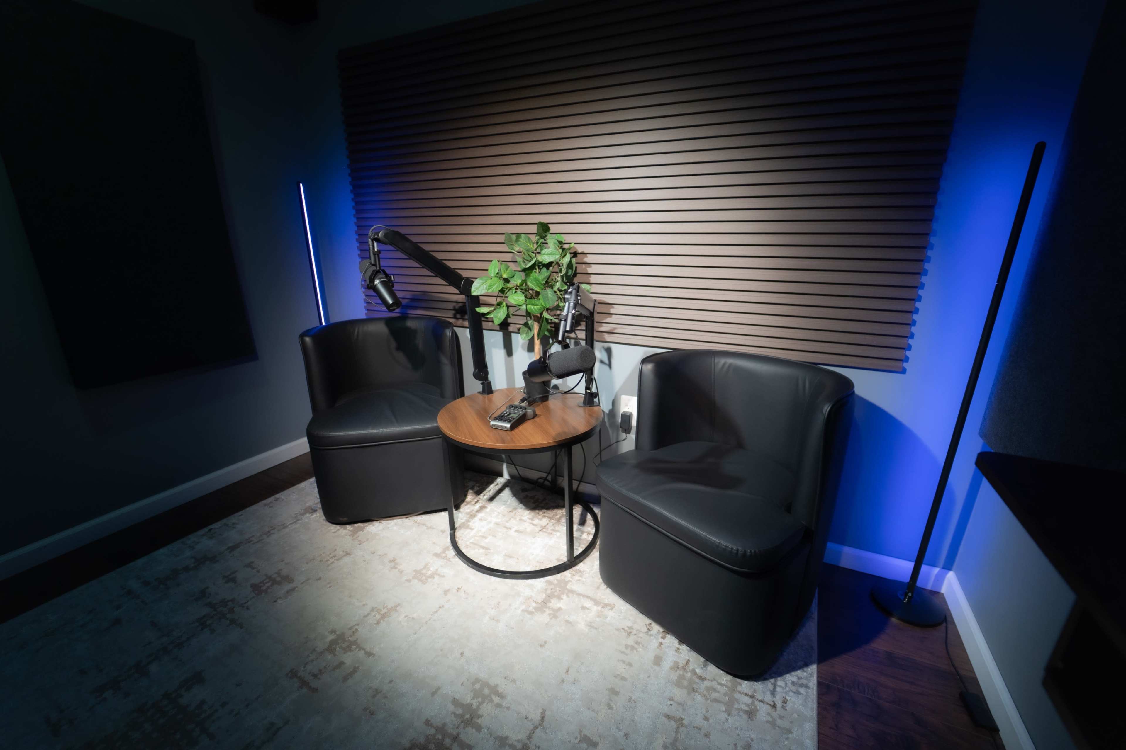 The image shows a cozy corner with two black chairs, a round table, and a small plant, illuminated by soft blue lighting against a textured wall.