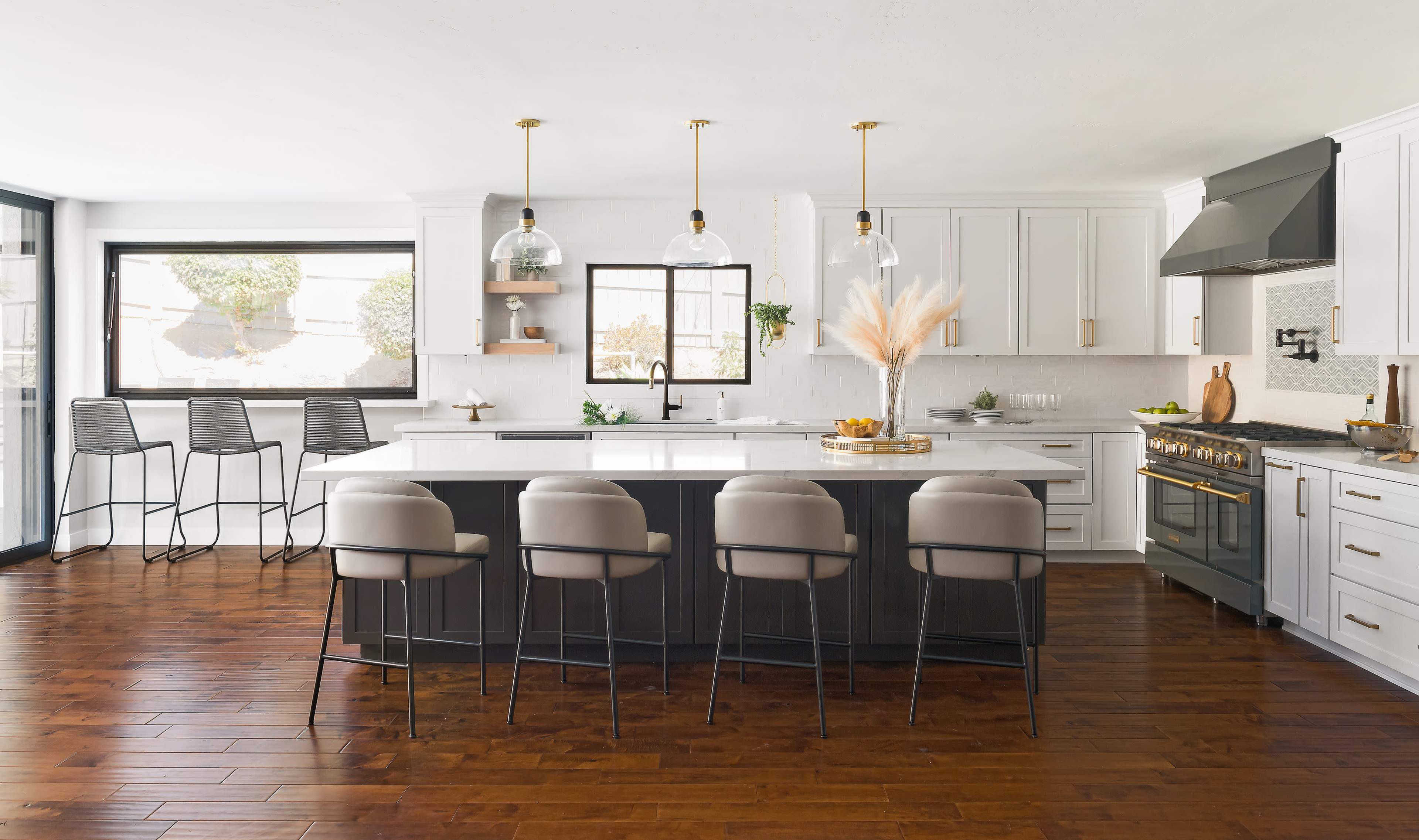 A modern kitchen features a central island with seated bar stools, pendant lighting, and a combination of white cabinetry and dark countertops.