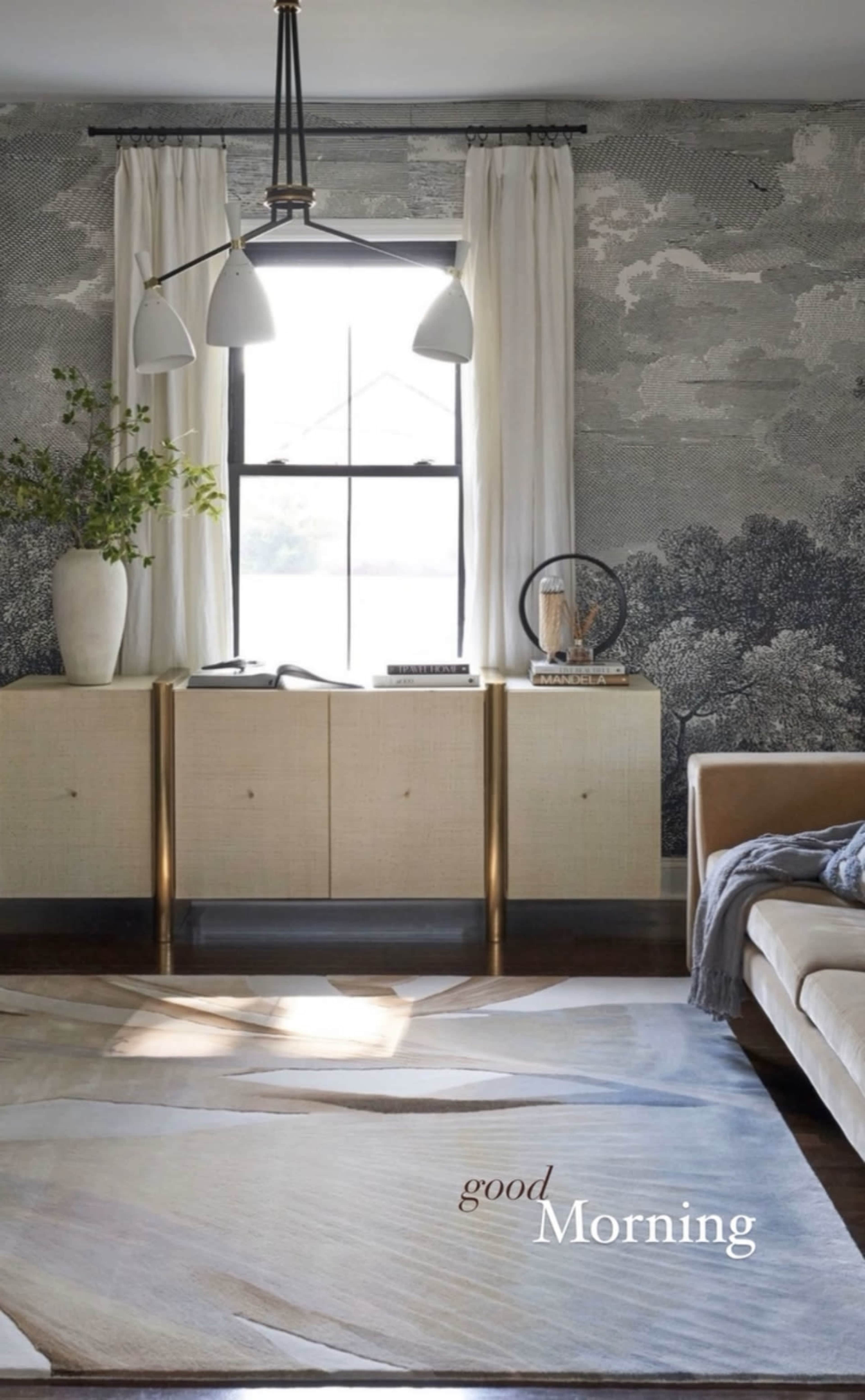 A living room features a large window with sheer curtains, a light-colored console table, and a rug with abstract patterns.
