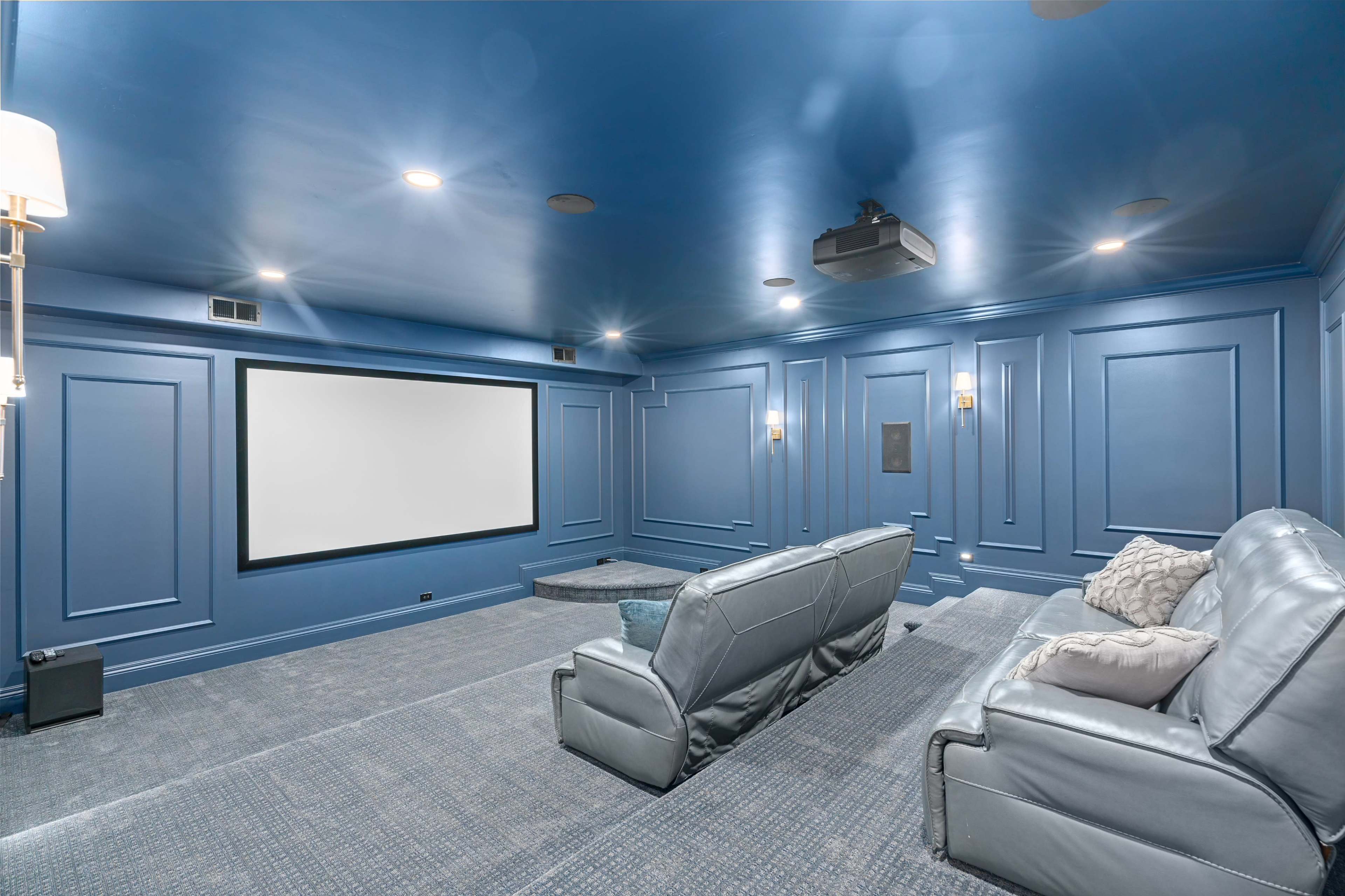 The image shows a home theater room featuring blue walls, a large screen, and comfortable leather seating arranged in front of the screen.