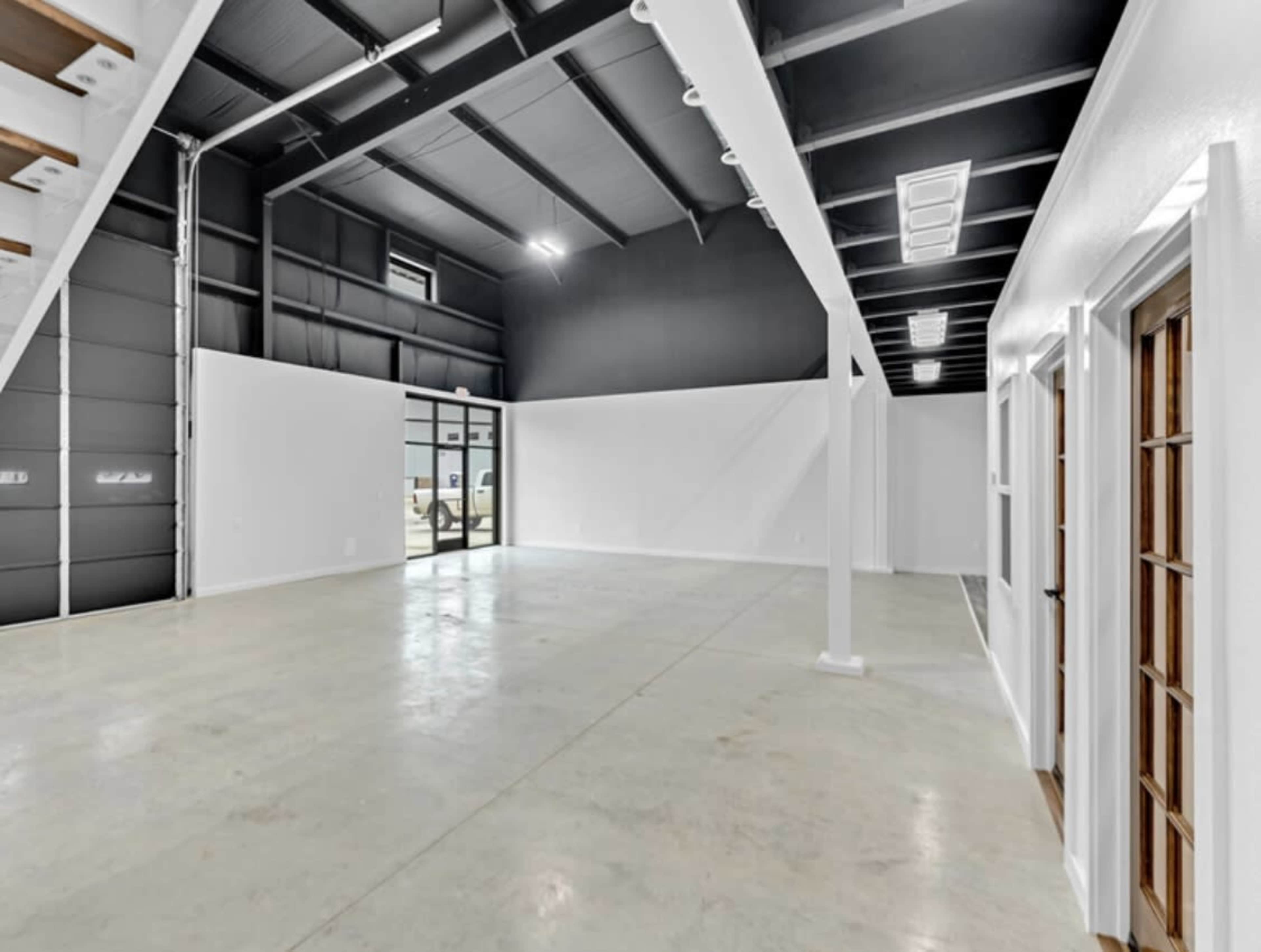 The image shows a spacious, empty interior of a building with high ceilings, concrete floors, and white walls.